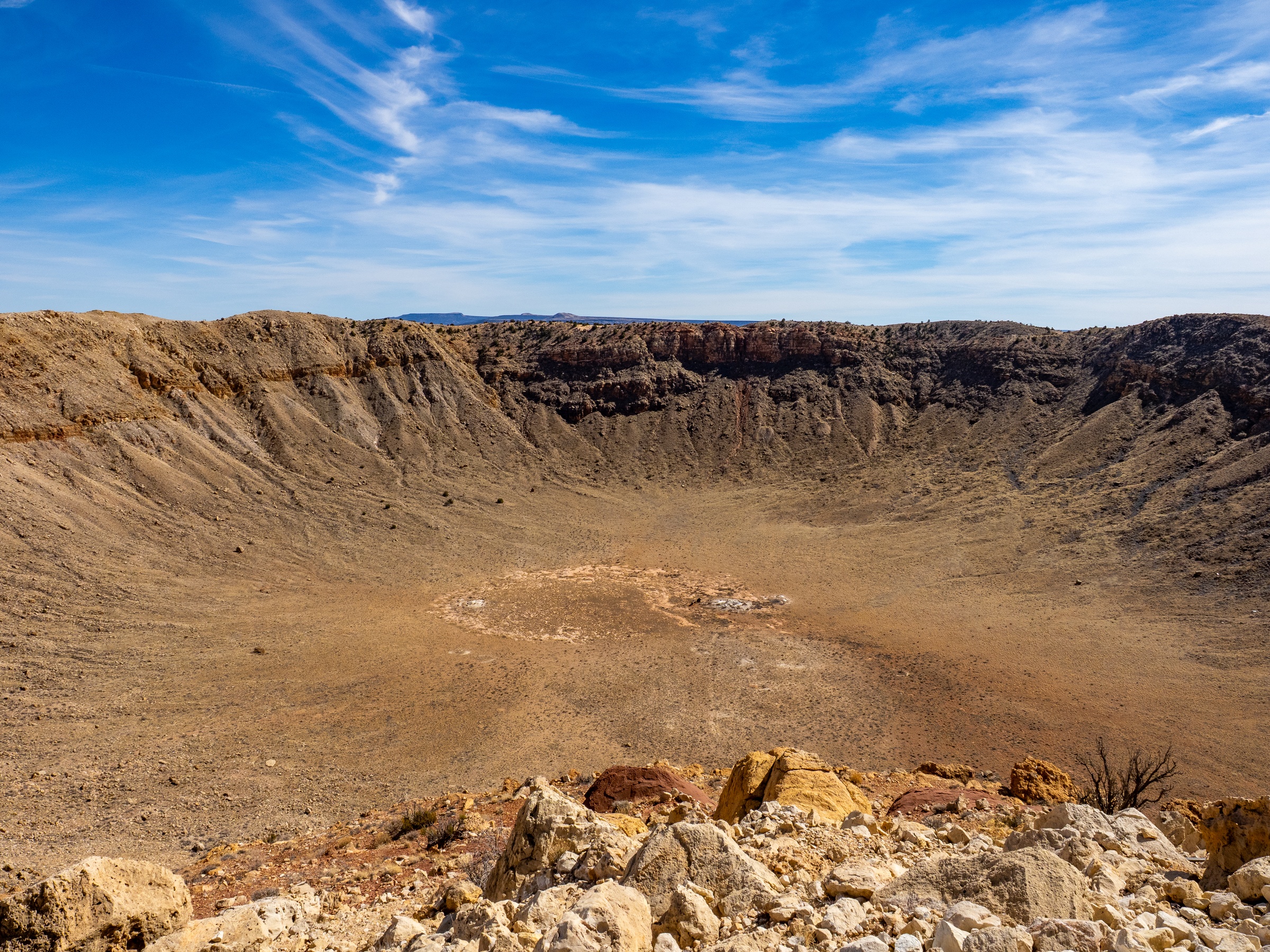 A large crater with dry, rocky slopes and a clear blue sky stretches across the landscape.