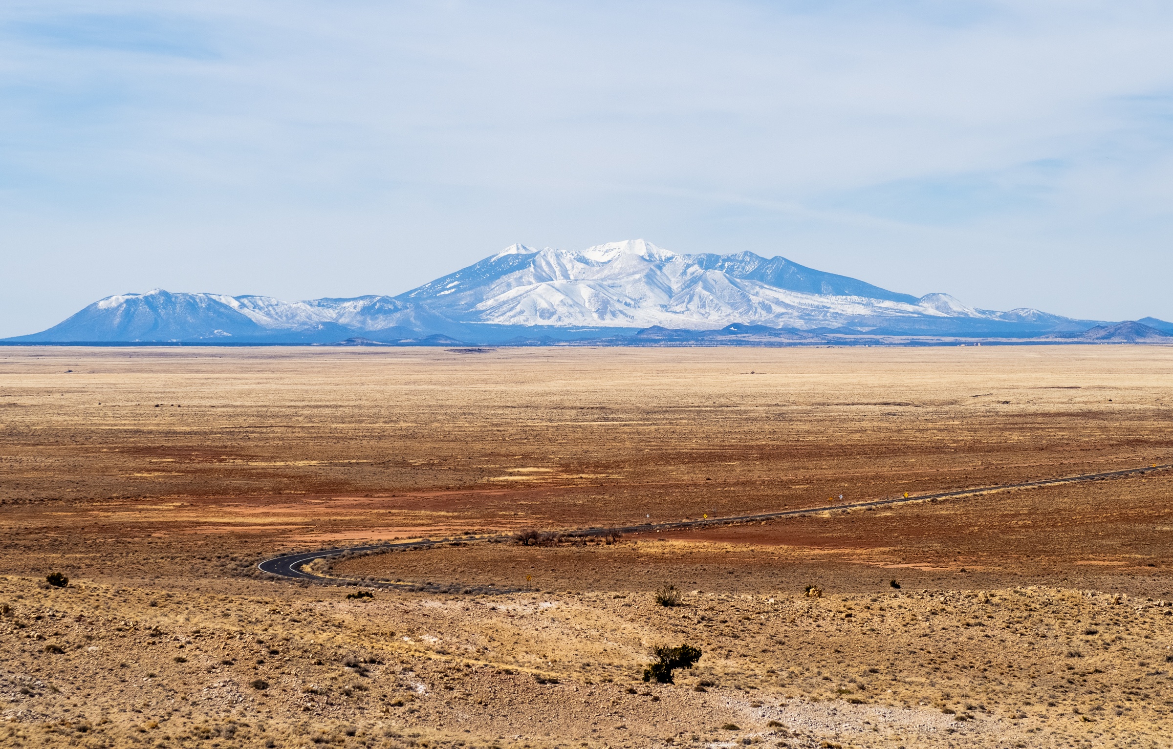 A snow-capped mountain rises above a vast, arid plain under a clear blue sky.