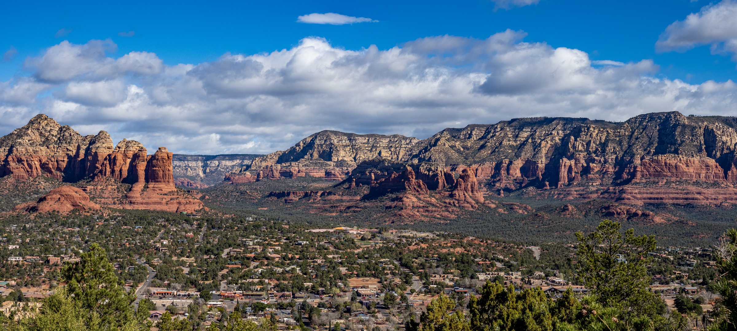 Red rock formations and a town are visible beneath a partly cloudy blue sky.