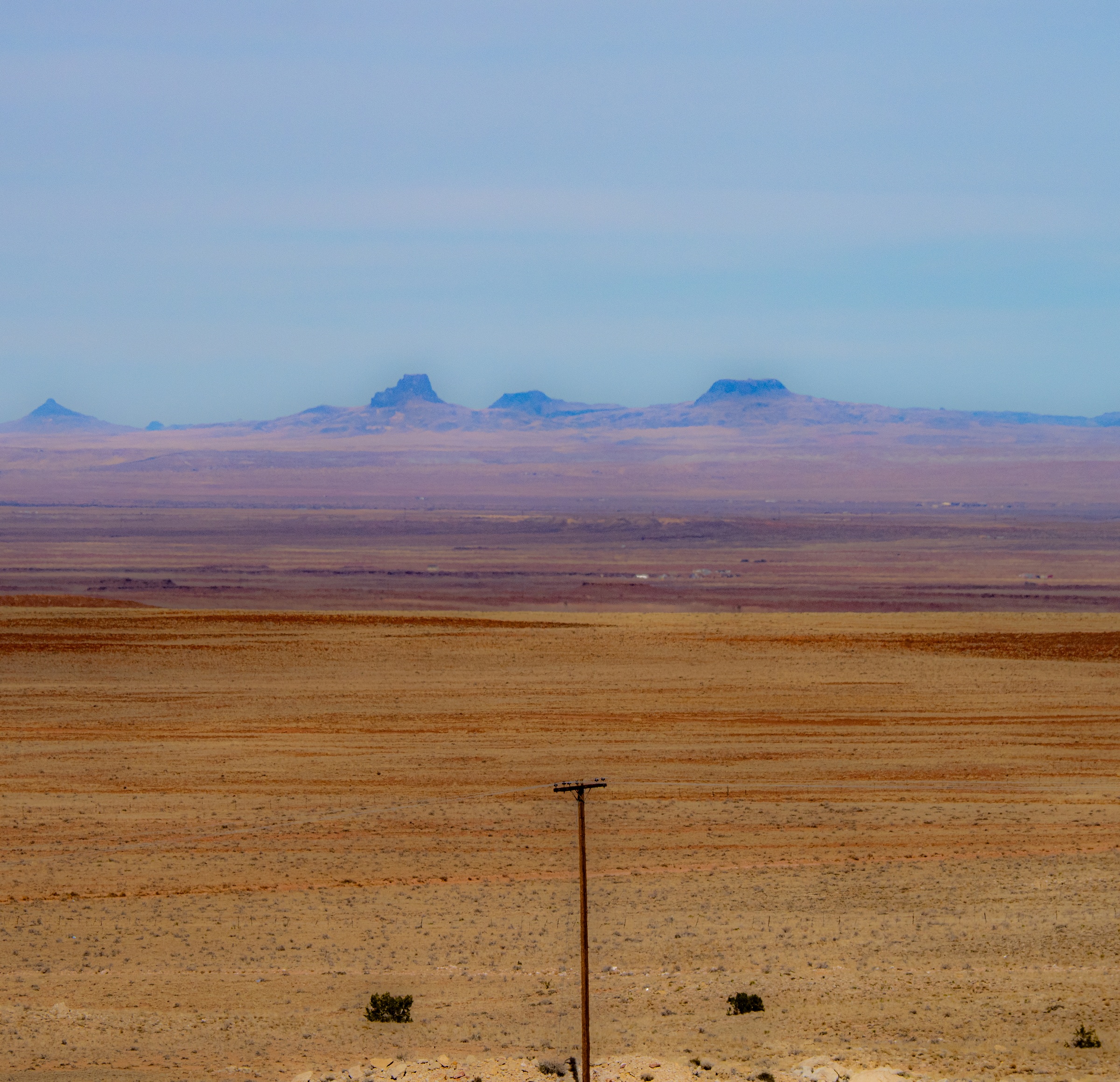 Vast desert landscape stretches to distant, hazy mountains under a pale blue sky.
