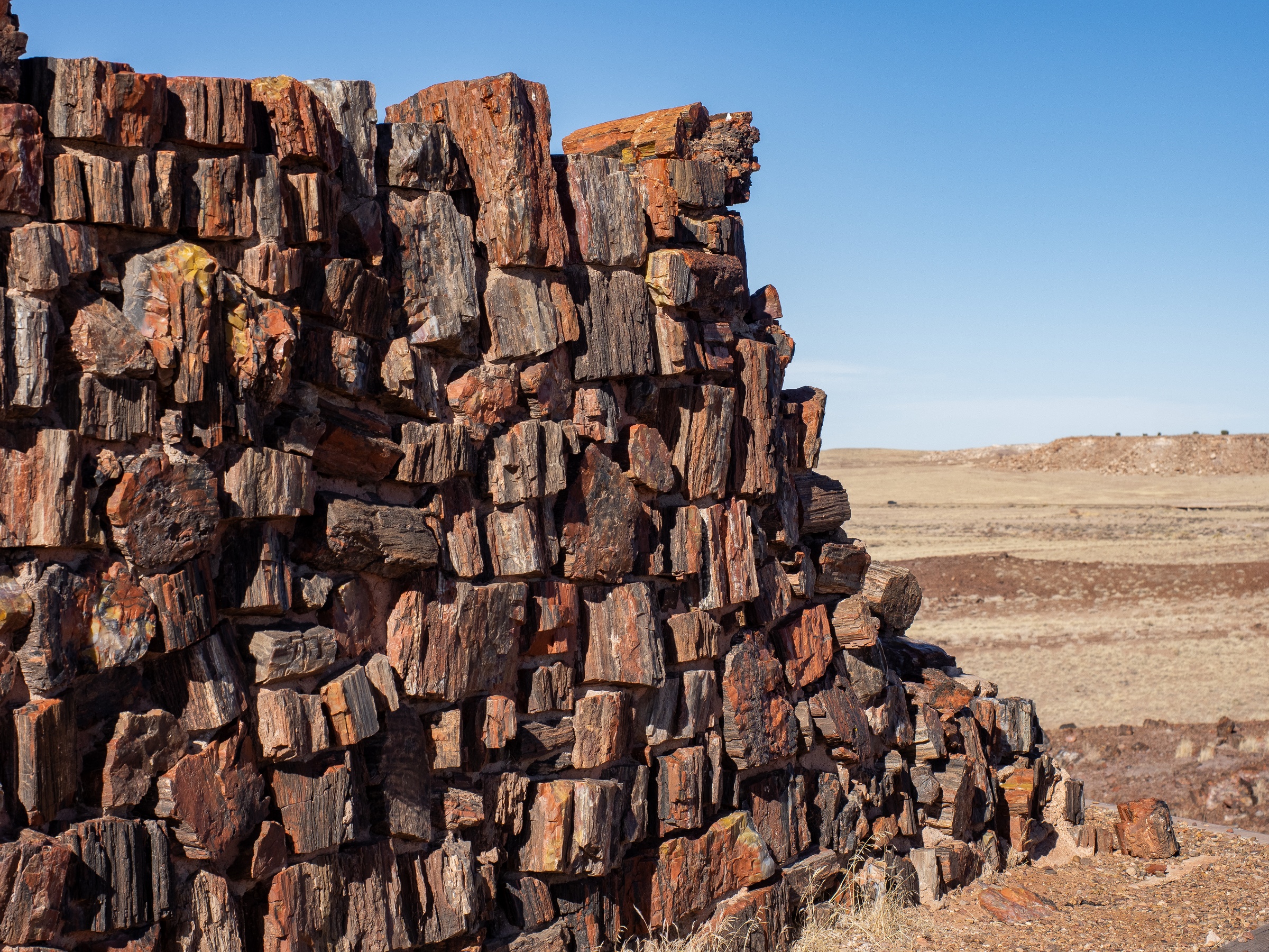 A weathered stone structure sits on a hillside overlooking a vast, arid landscape under a clear sky.