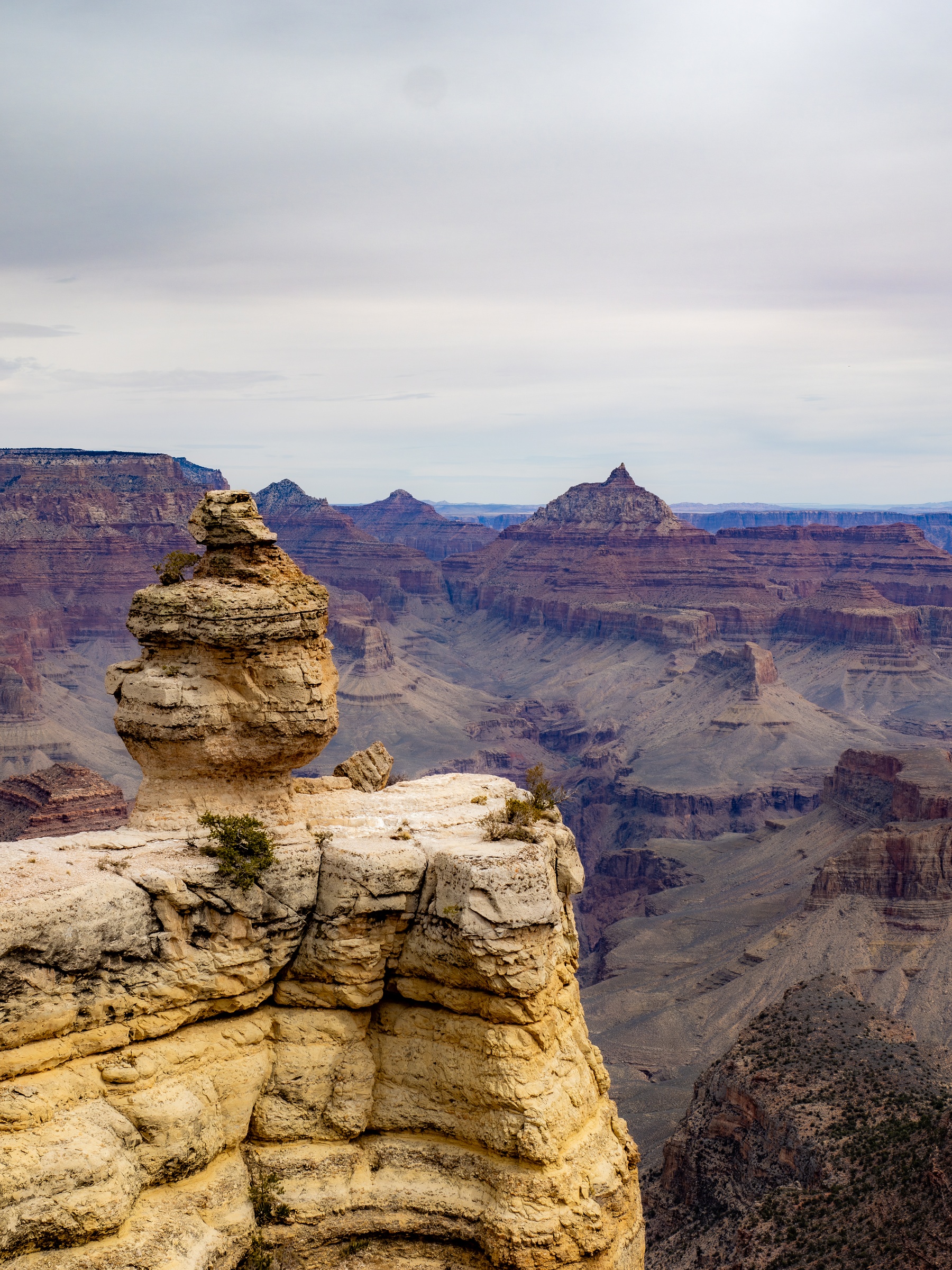A sandstone rock formation overlooks a vast canyon landscape with layered cliffs and distant peaks.