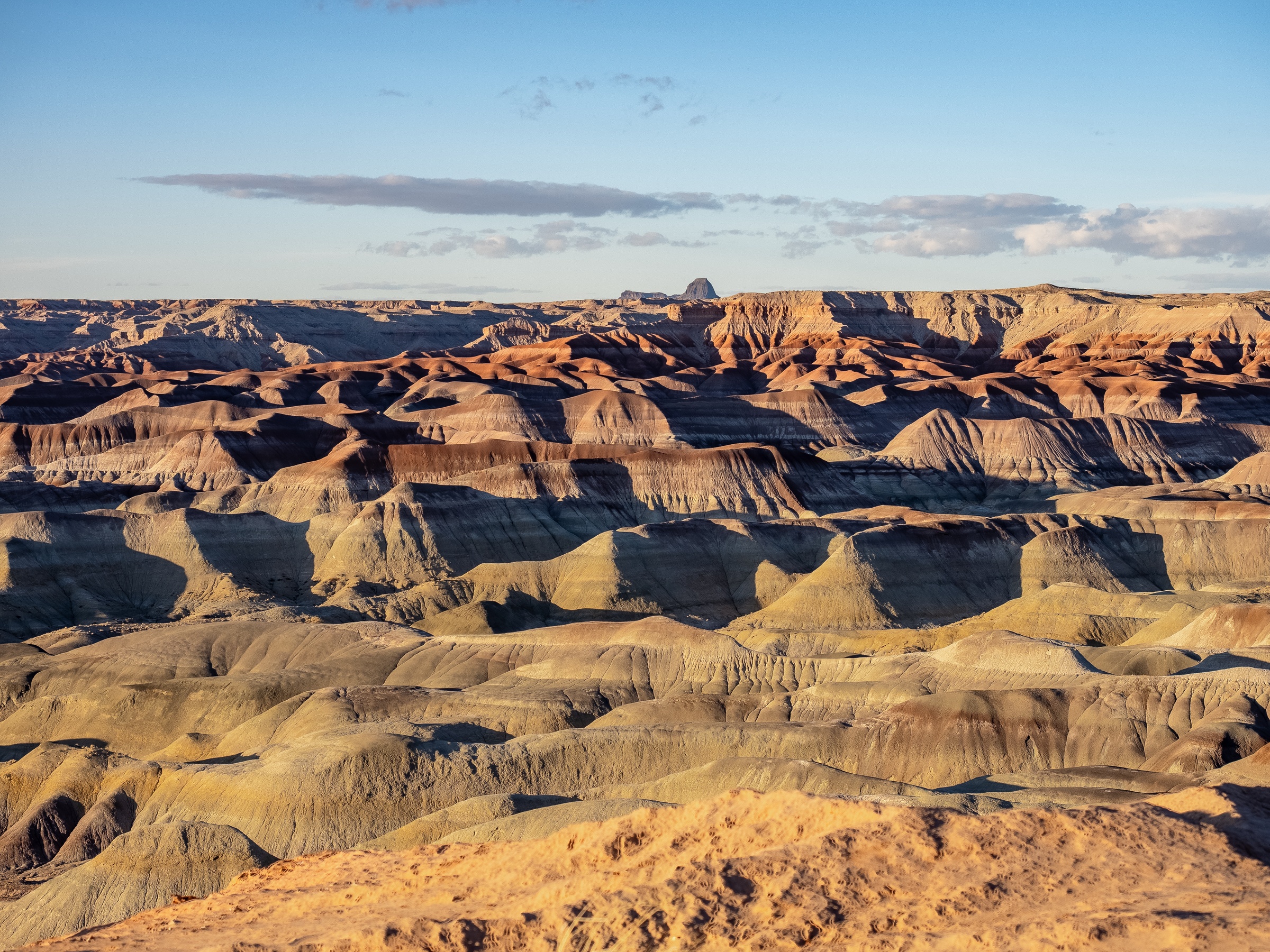 Vast eroded badlands display layered rock formations under a partly cloudy sky.