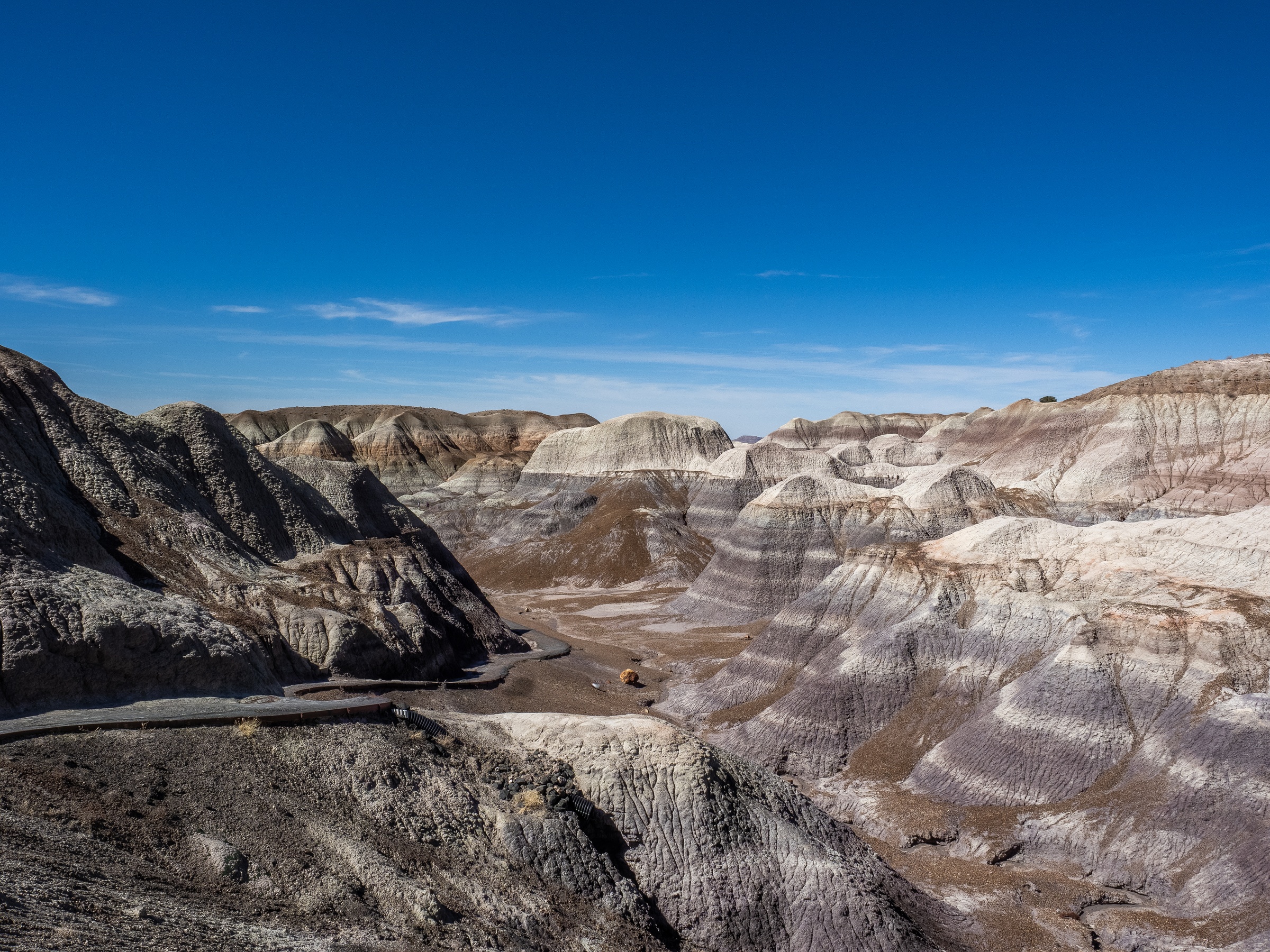 Colorful layered rock formations fill a vast canyon under a clear blue sky.