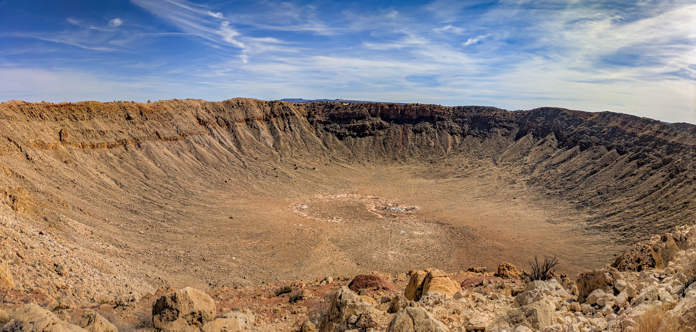 A large, circular crater with eroded walls and sparse vegetation sits under a partly cloudy sky.