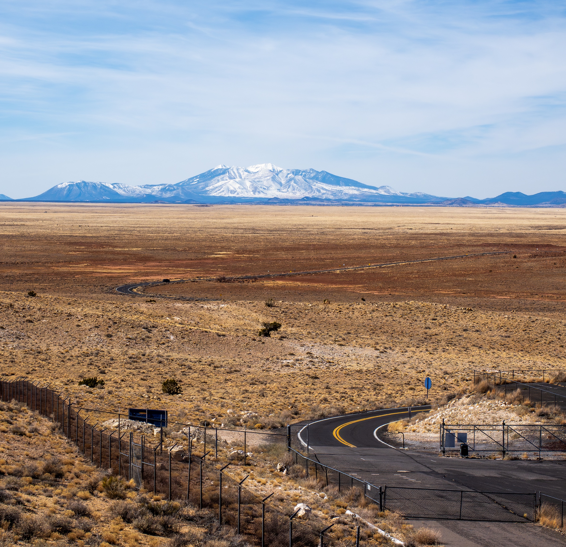 A winding road leads toward a snow-capped mountain range across a vast, arid landscape.