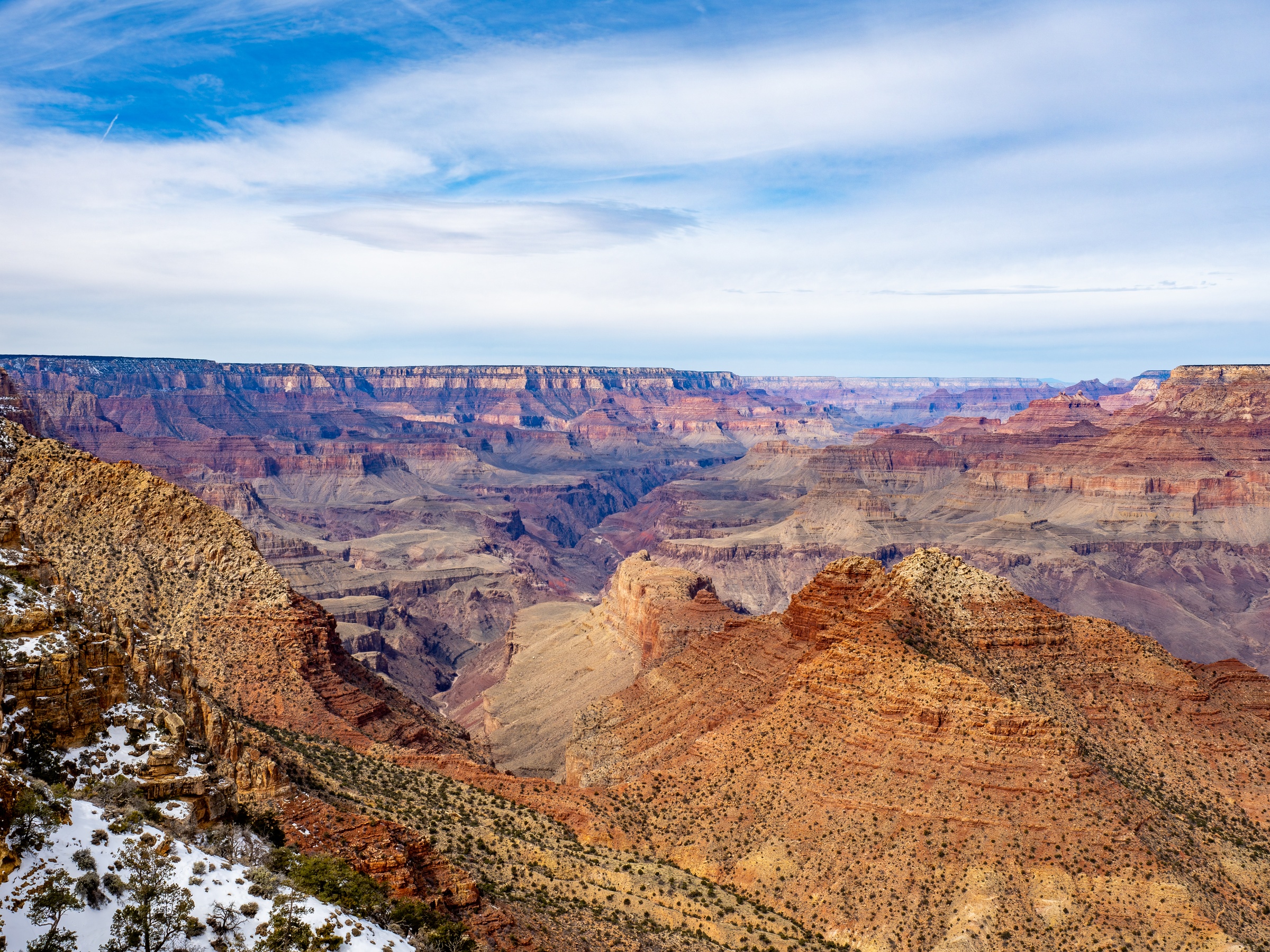 Vast layered canyon walls and mesas dominate a landscape under a cloudy sky.