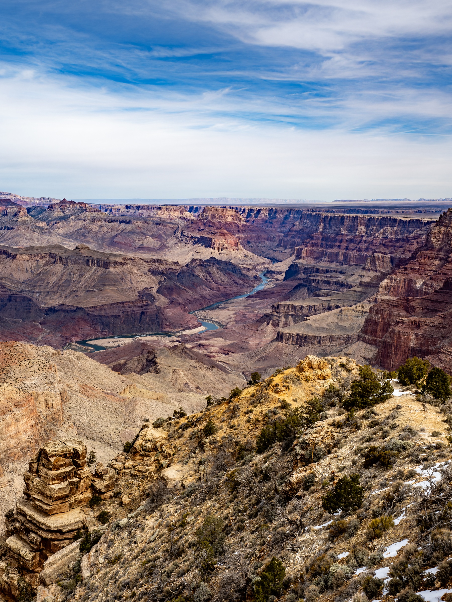 Vast canyon walls and a winding river stretch beneath a partly cloudy blue sky.