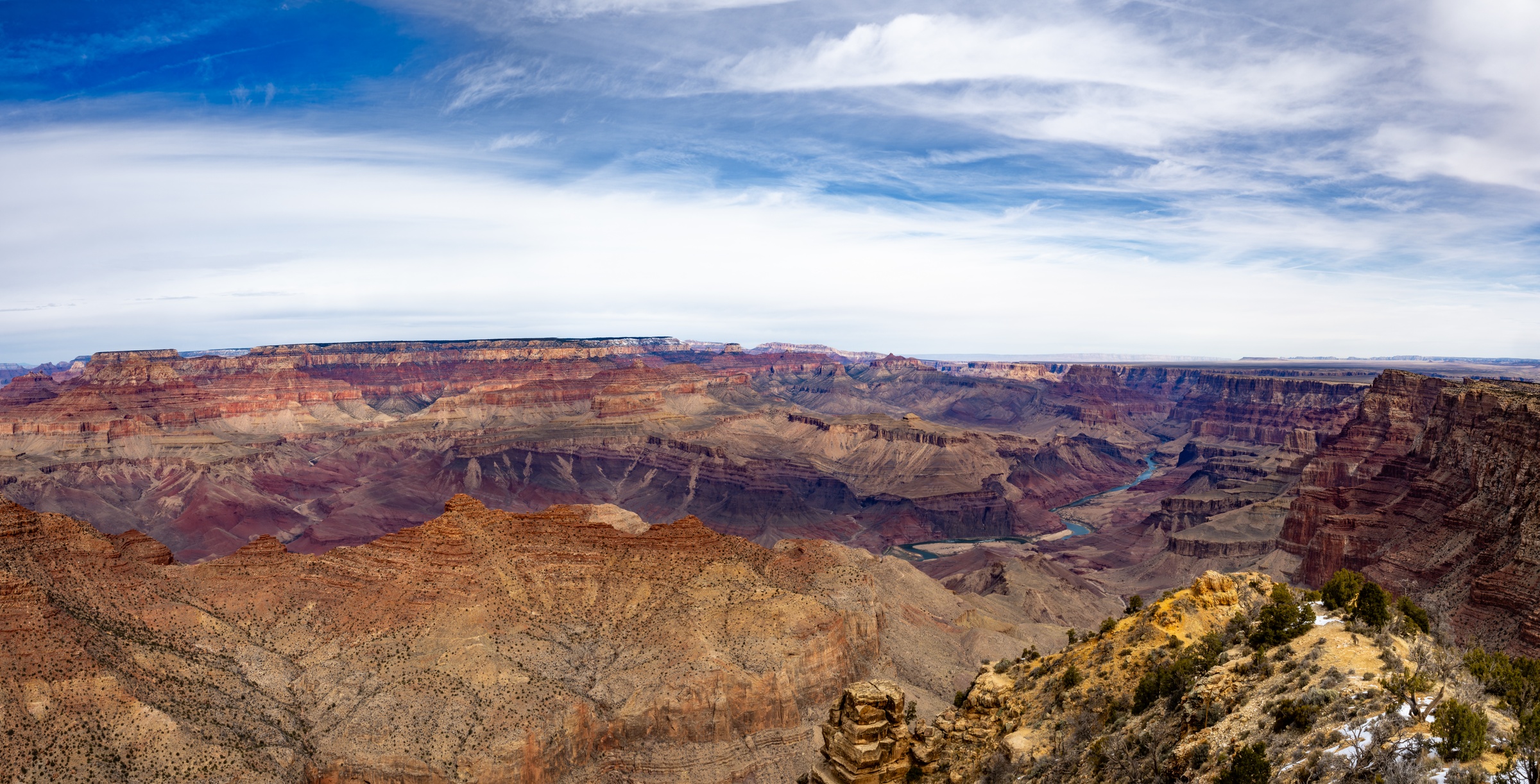 Vast canyon walls of layered rock and desert vegetation stretch under a cloudy sky.
