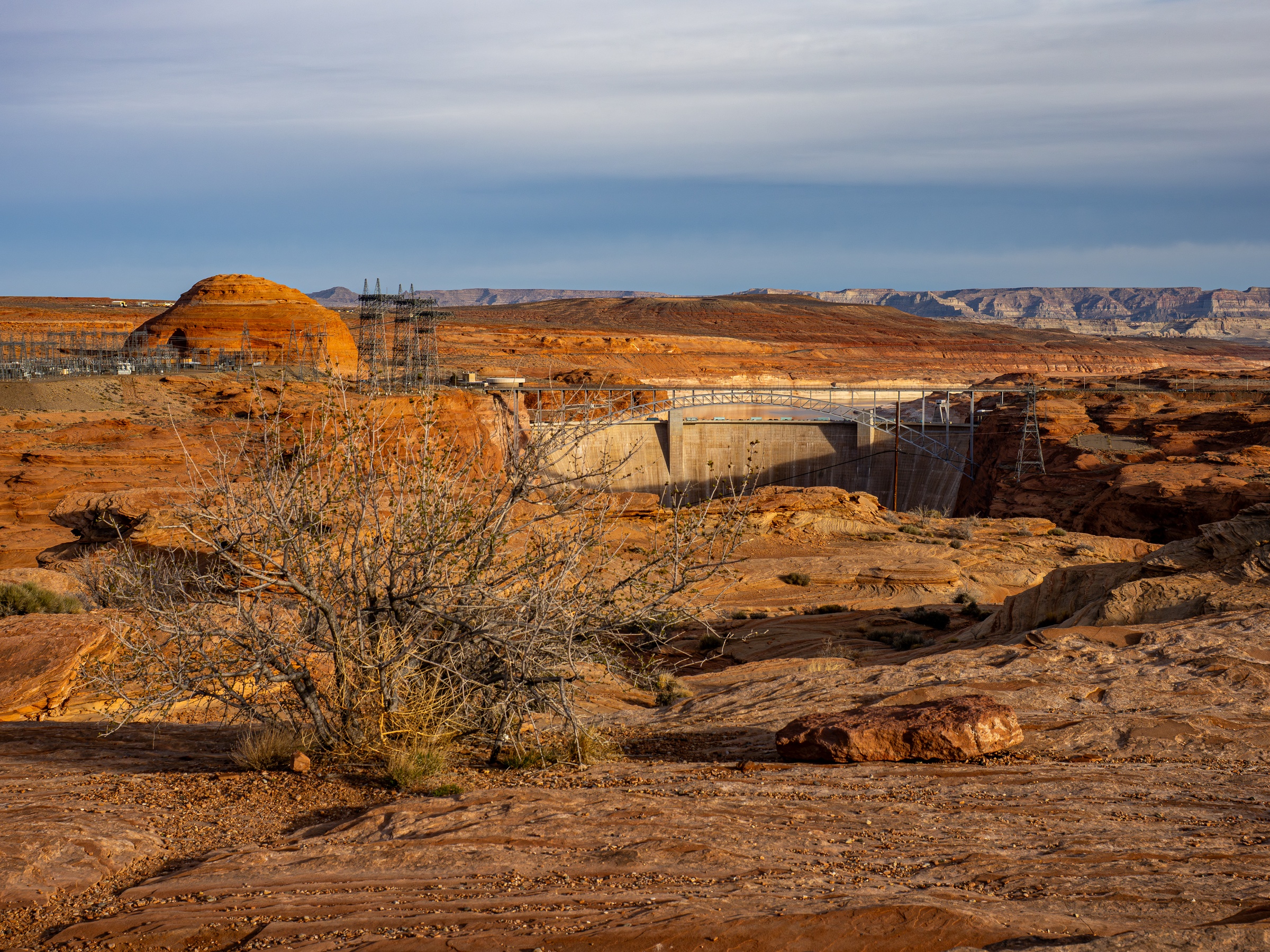 A dam and construction site sit within a vast, arid landscape of red rock formations.