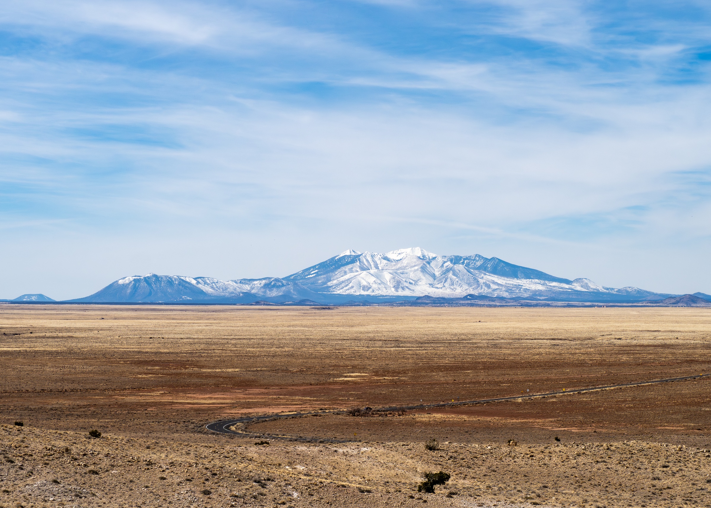 Snow-capped mountains rise above a vast, arid plain under a clear blue sky.