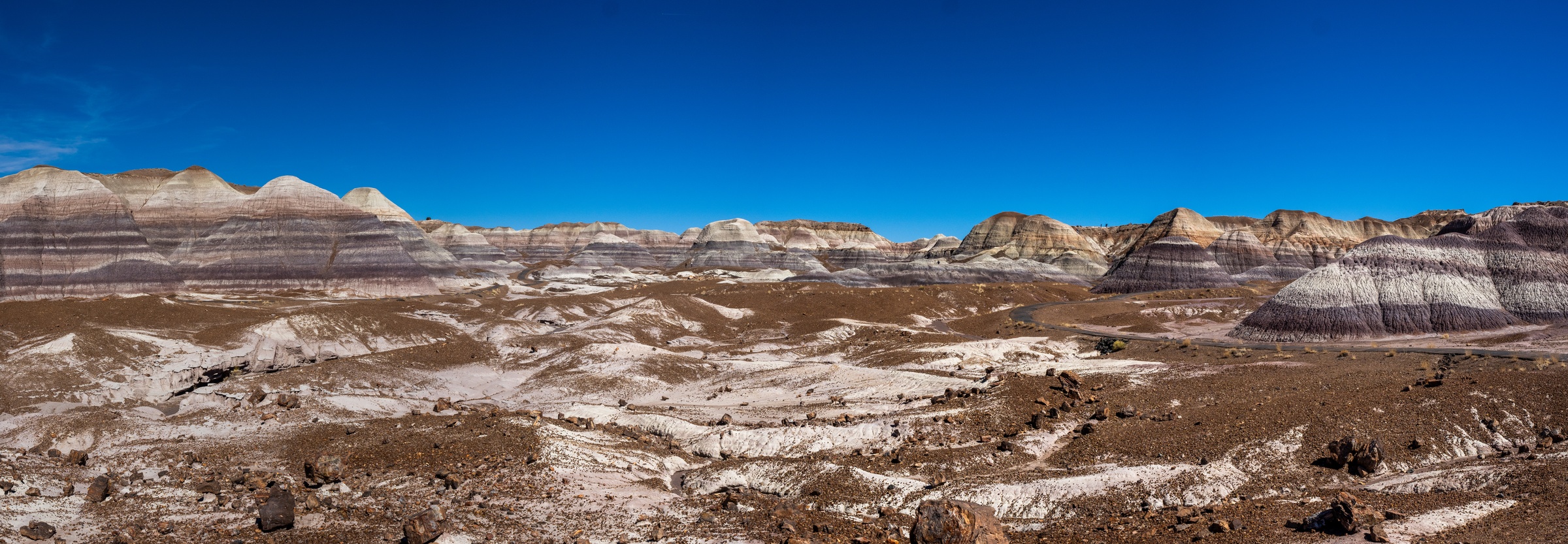Vast eroded badlands display layered rock formations under a clear blue sky.