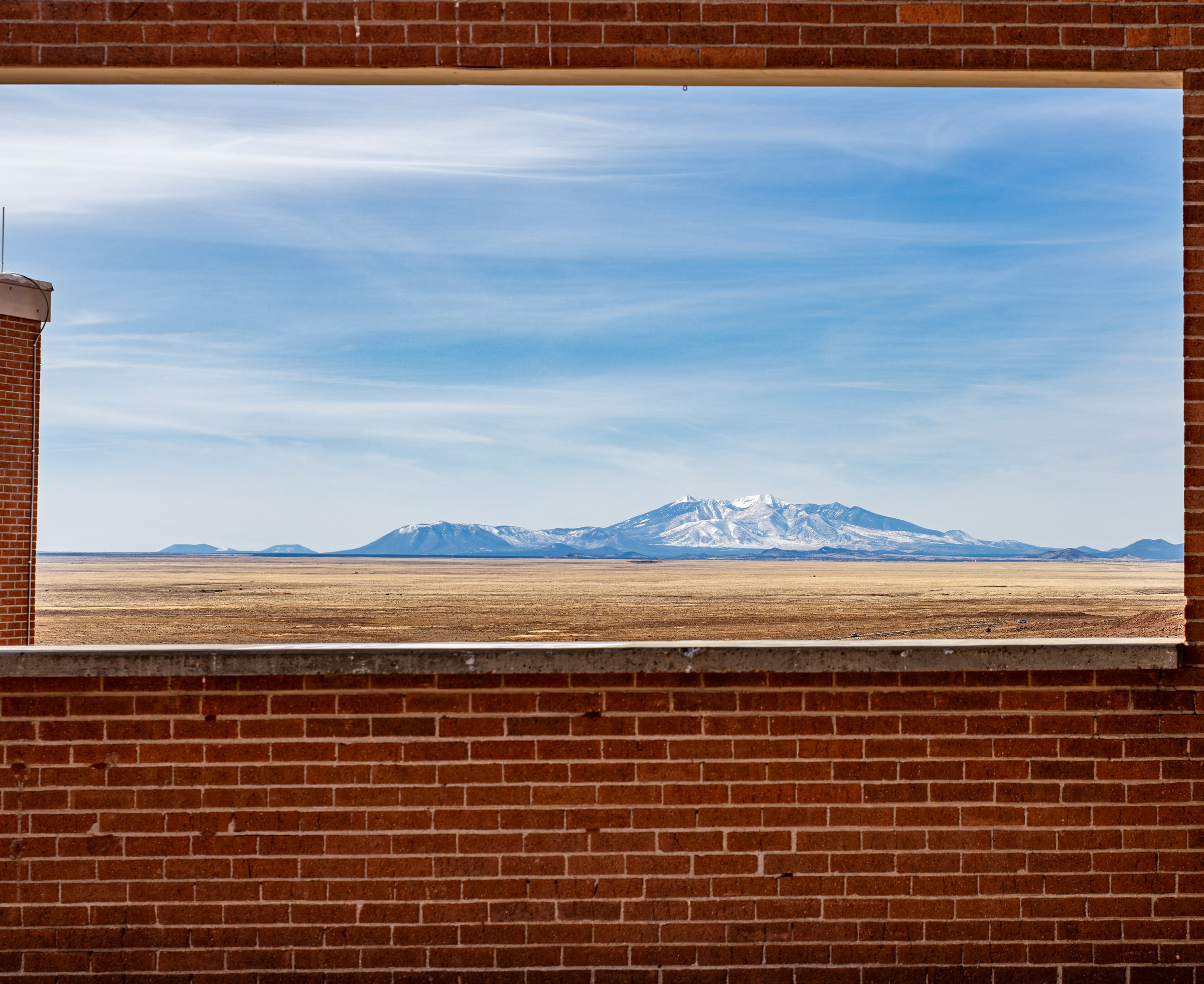 A window frames a distant mountain range over a flat, dry landscape under a cloudy sky.