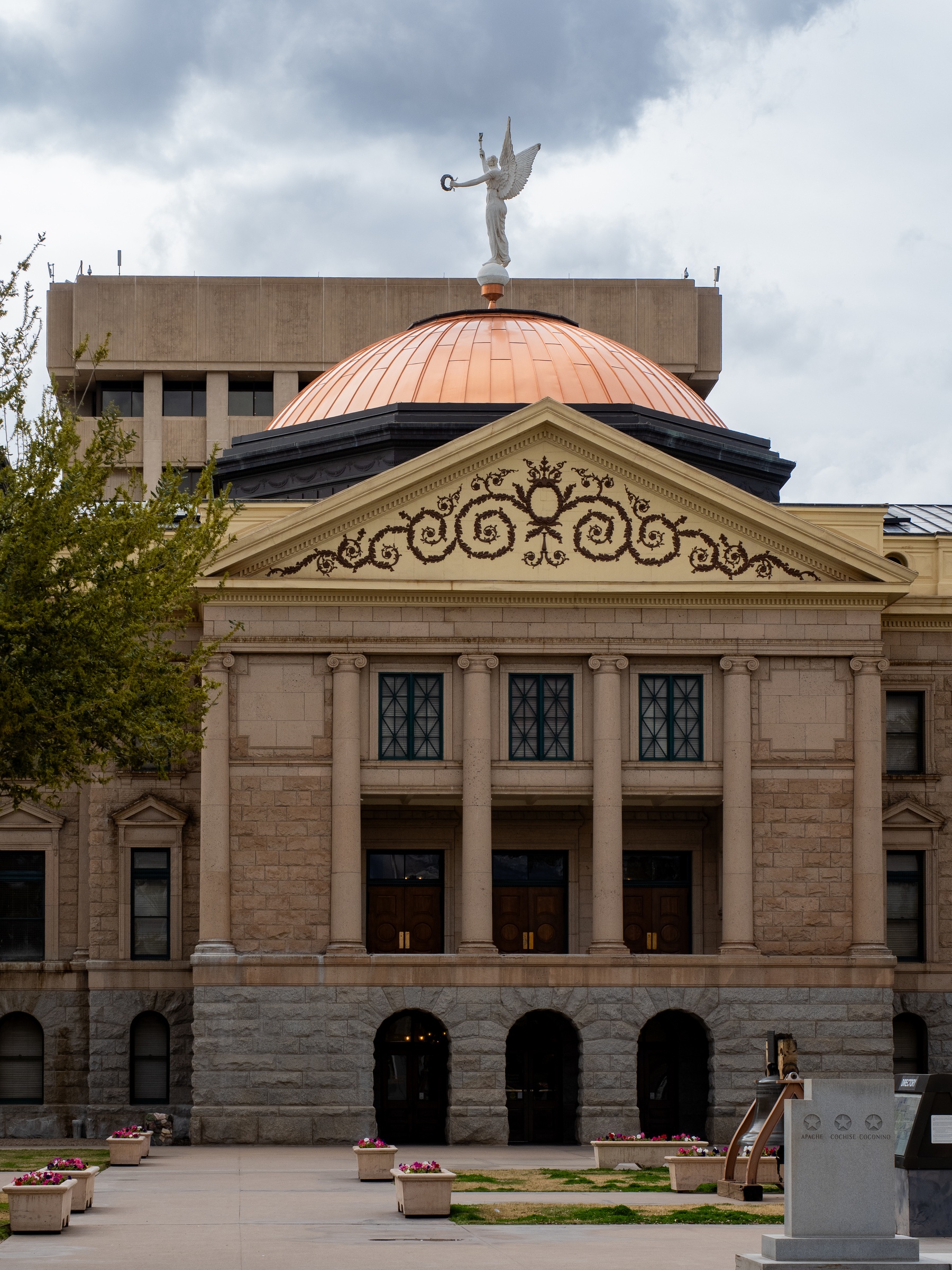 A copper-domed building with a statue on top sits against a cloudy sky.