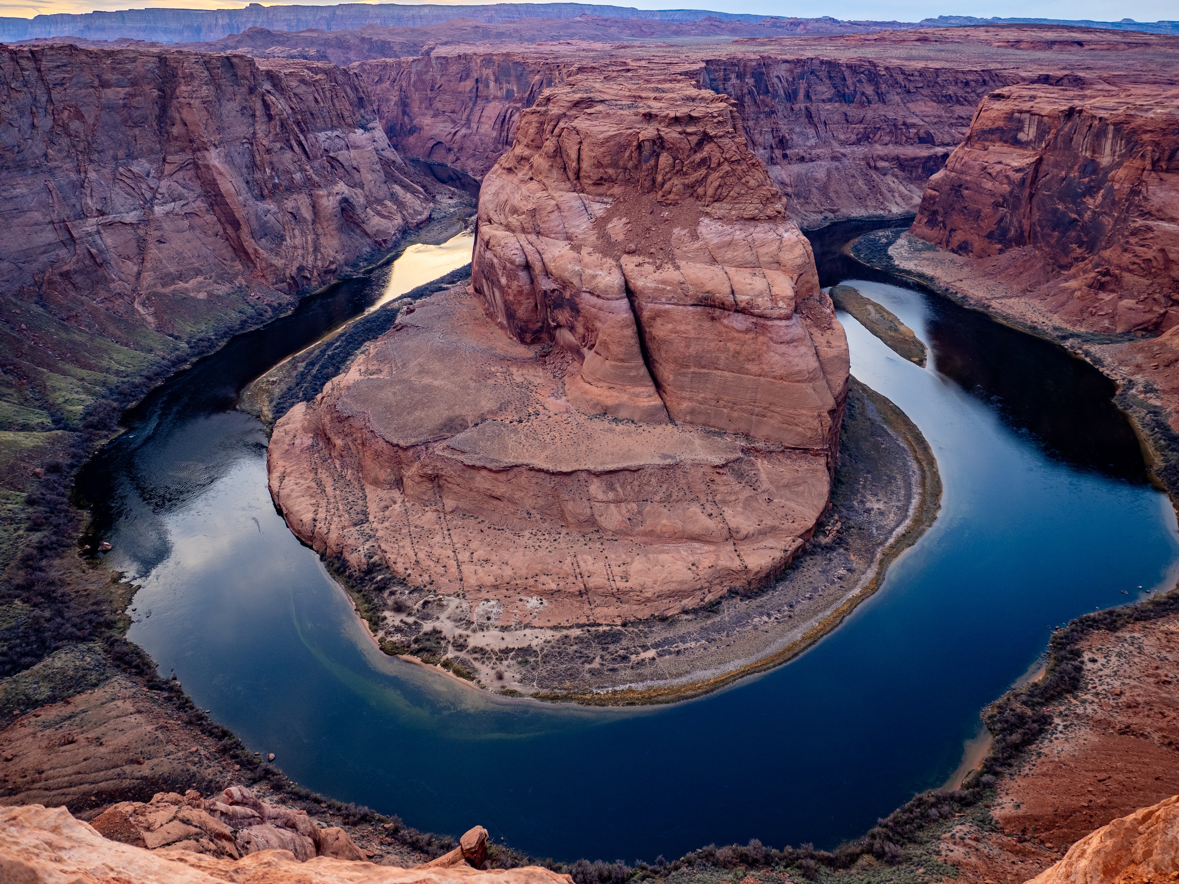 Horseshoe Bend curves along a river with a large sandstone butte rising above it.