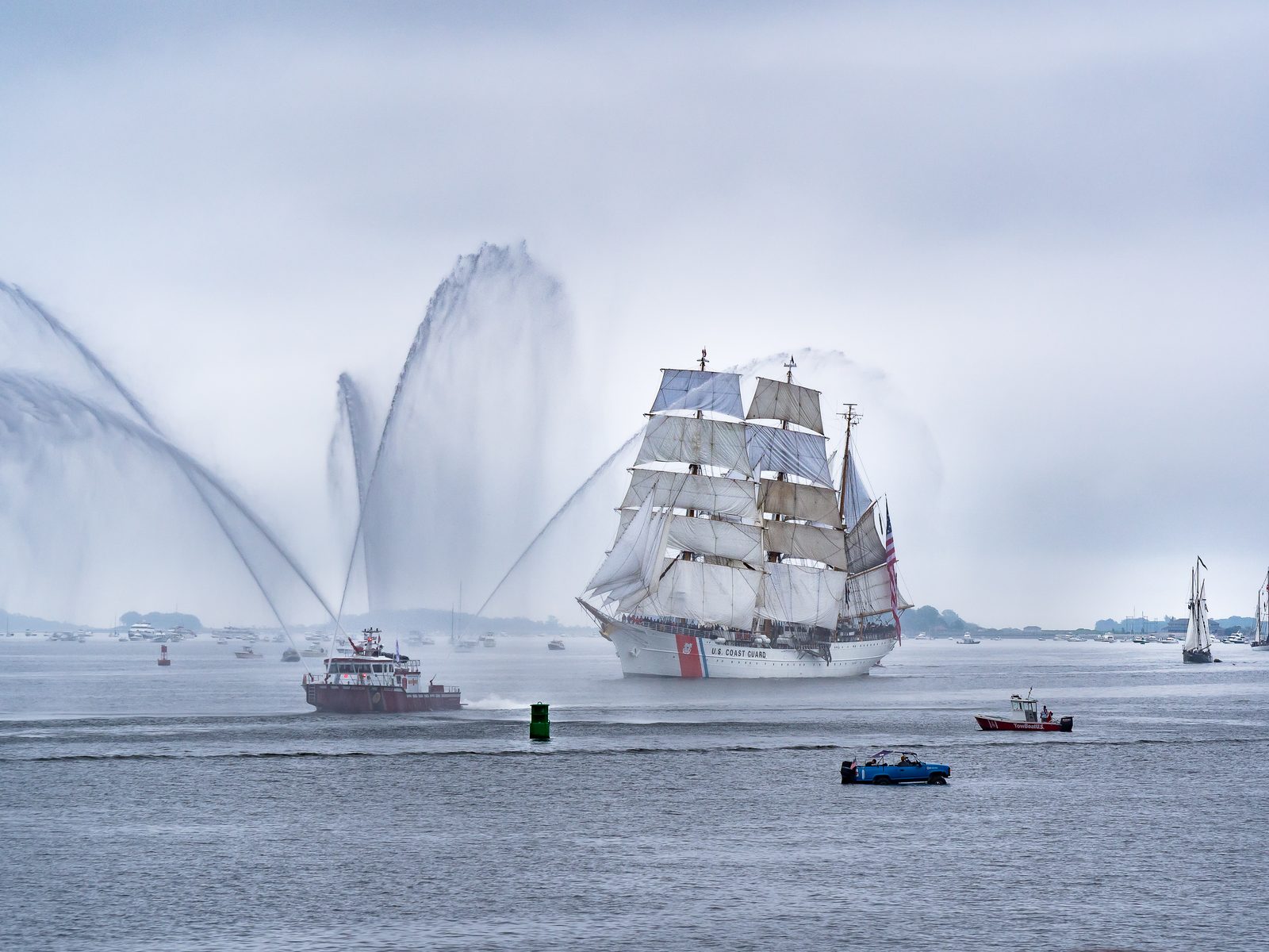 A tall sail ship follows a firefighting ship in Boston Harbor
