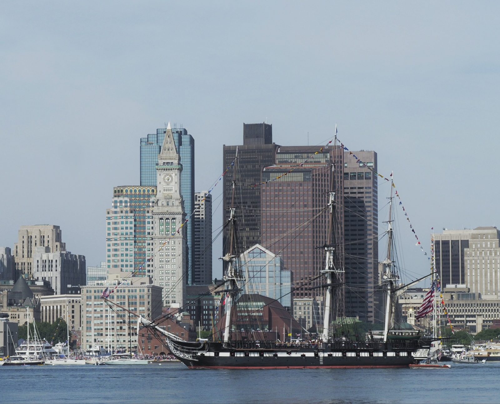 A large sailing ship floats on the water before a city skyline with tall buildings.