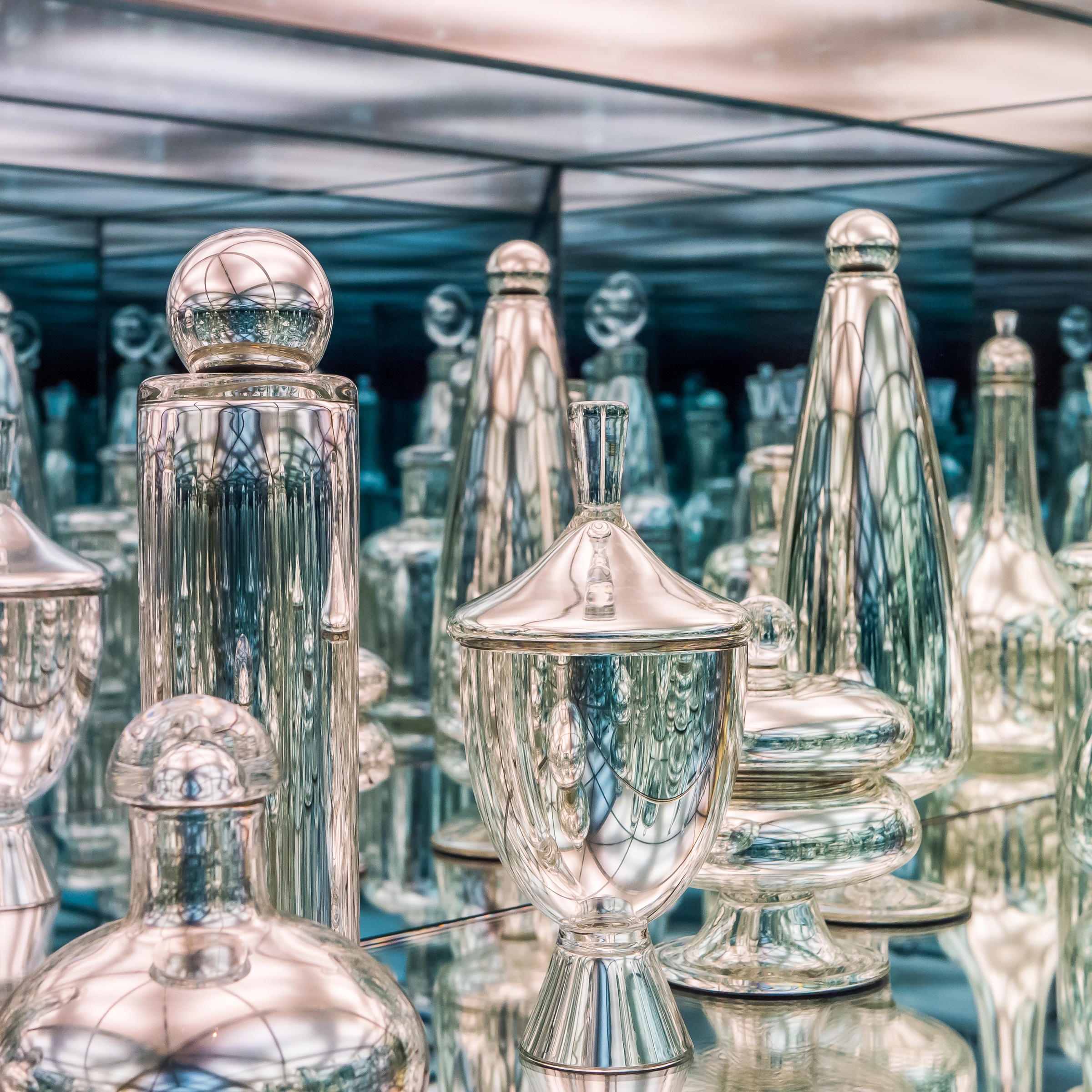 Silver perfume bottles and containers are reflected in a mirrored room.
