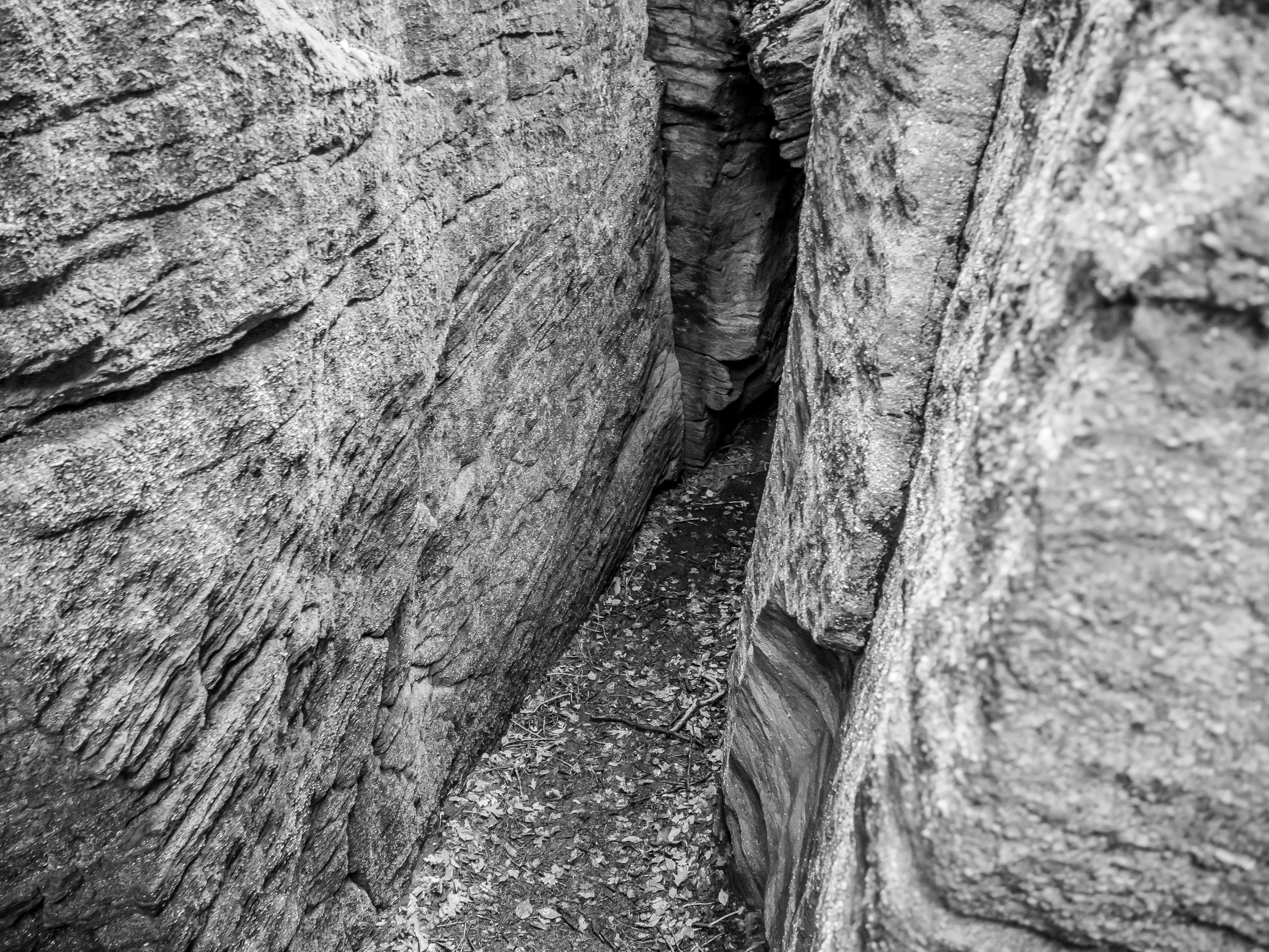 Narrow canyon walls of layered rock converge, creating a shadowed passage along a rocky ground.