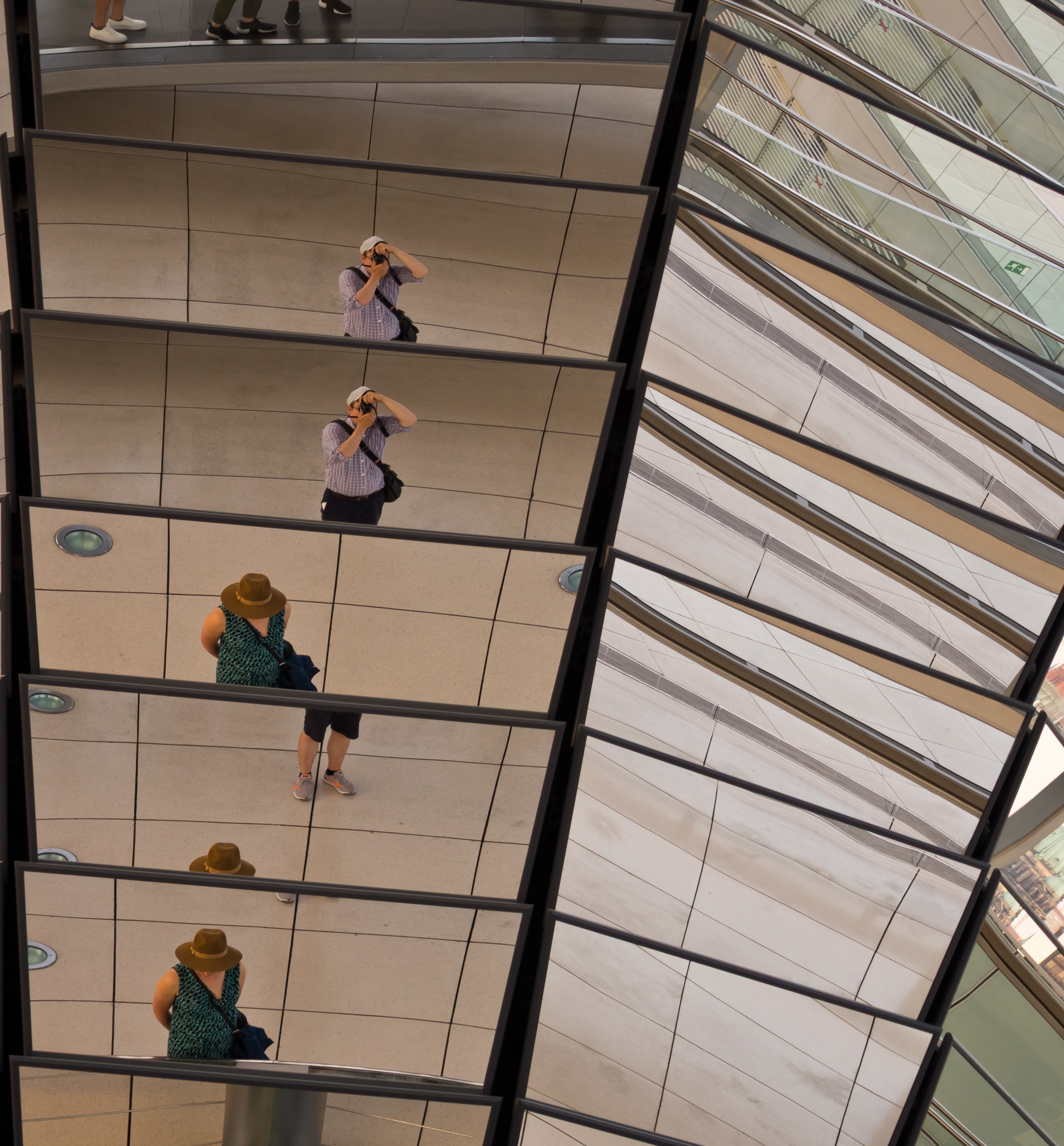A person in a hat takes photos within the reflective, layered architecture of a modern building.