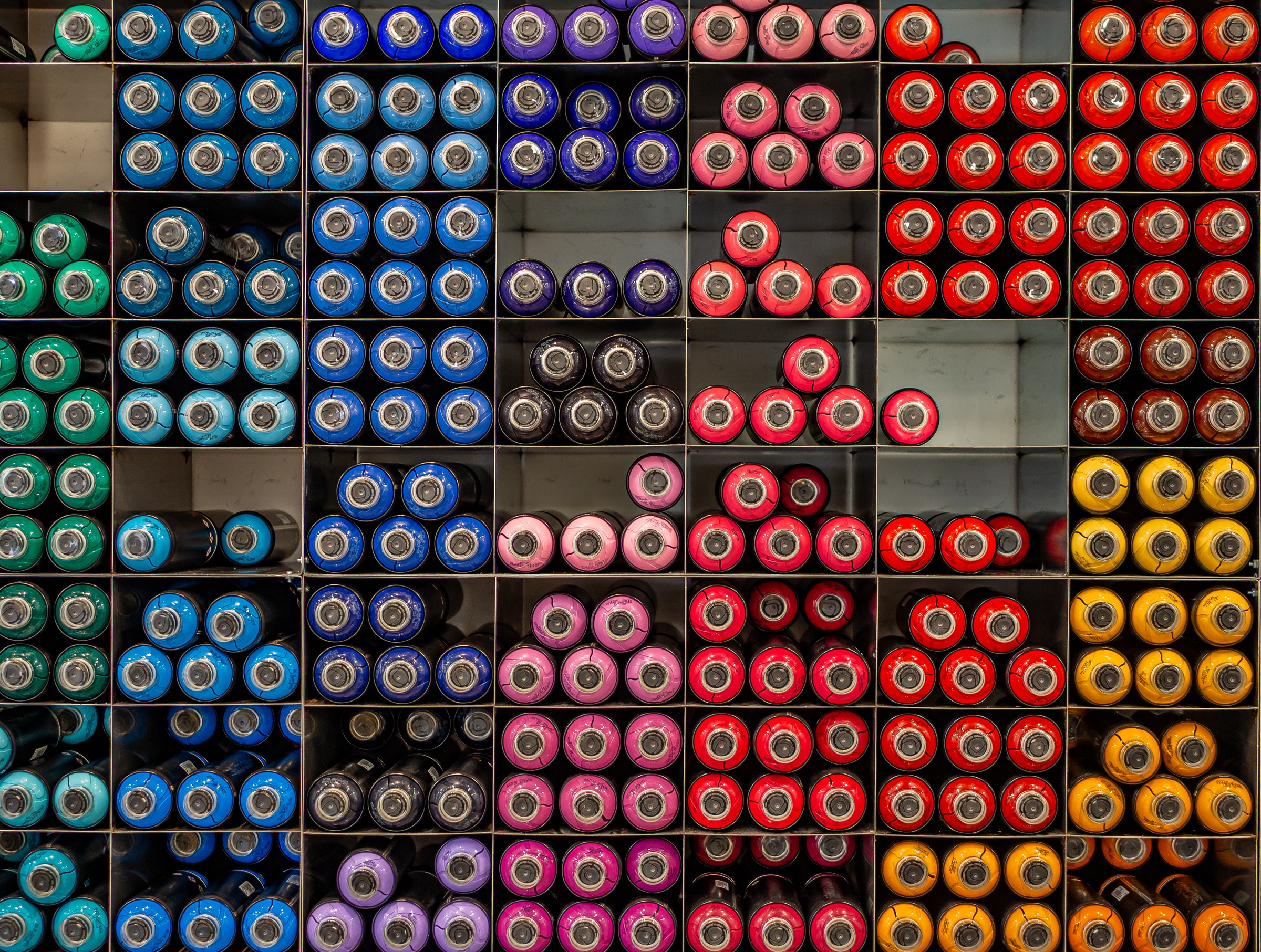Shelves display rows of colorful spray paint cans, neatly organized by color.