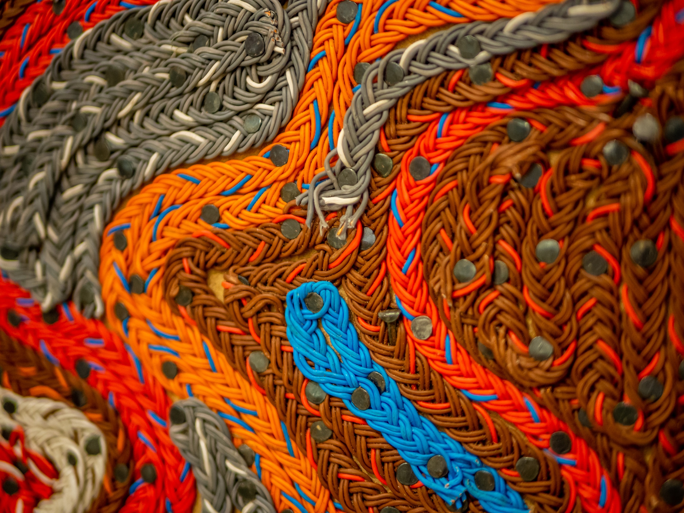 Colorful rubber bands are braided and woven into a textured, abstract design.