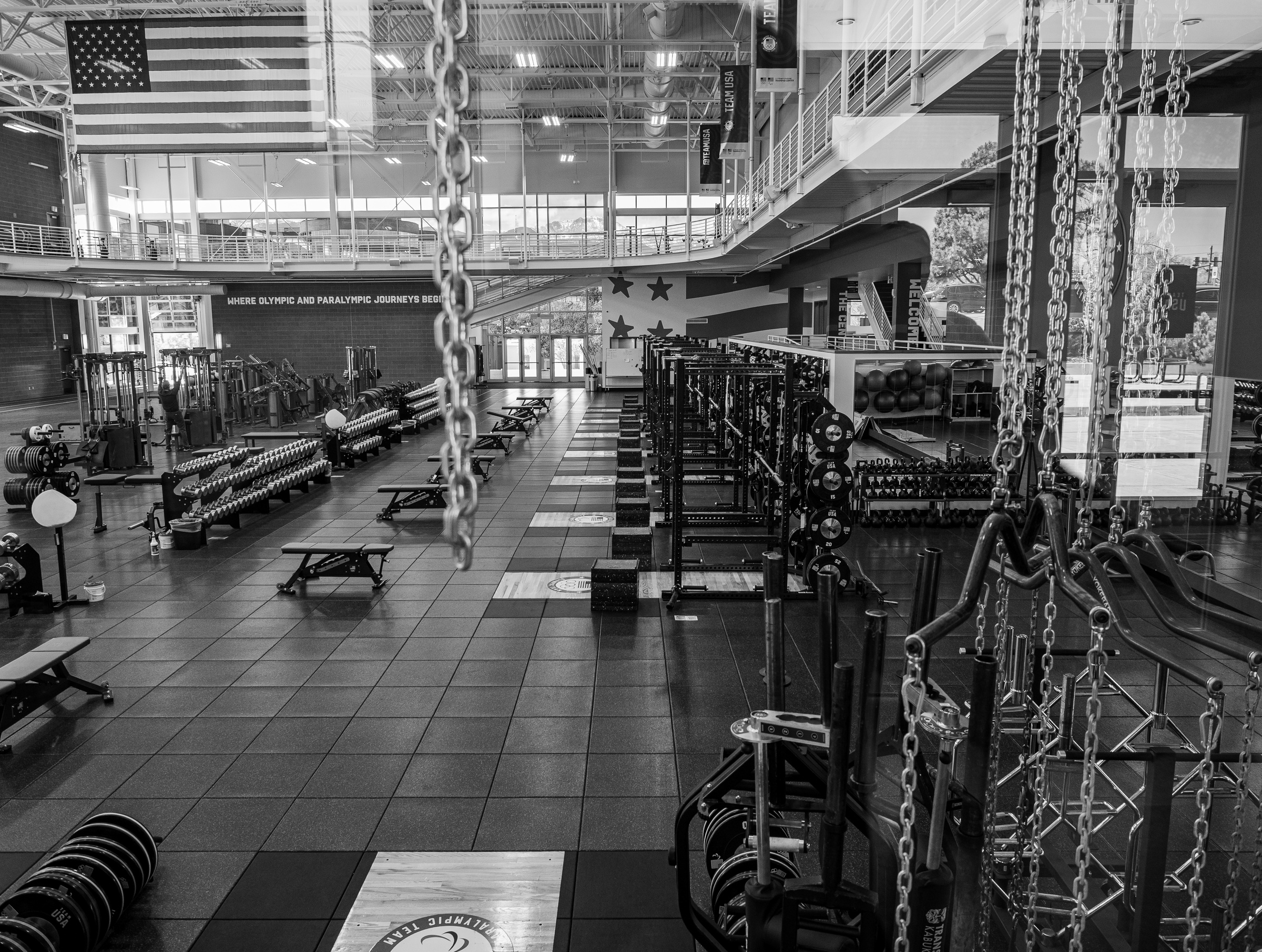 A large gym with weight racks, benches, and climbing ropes fills a spacious black-and-white interior.