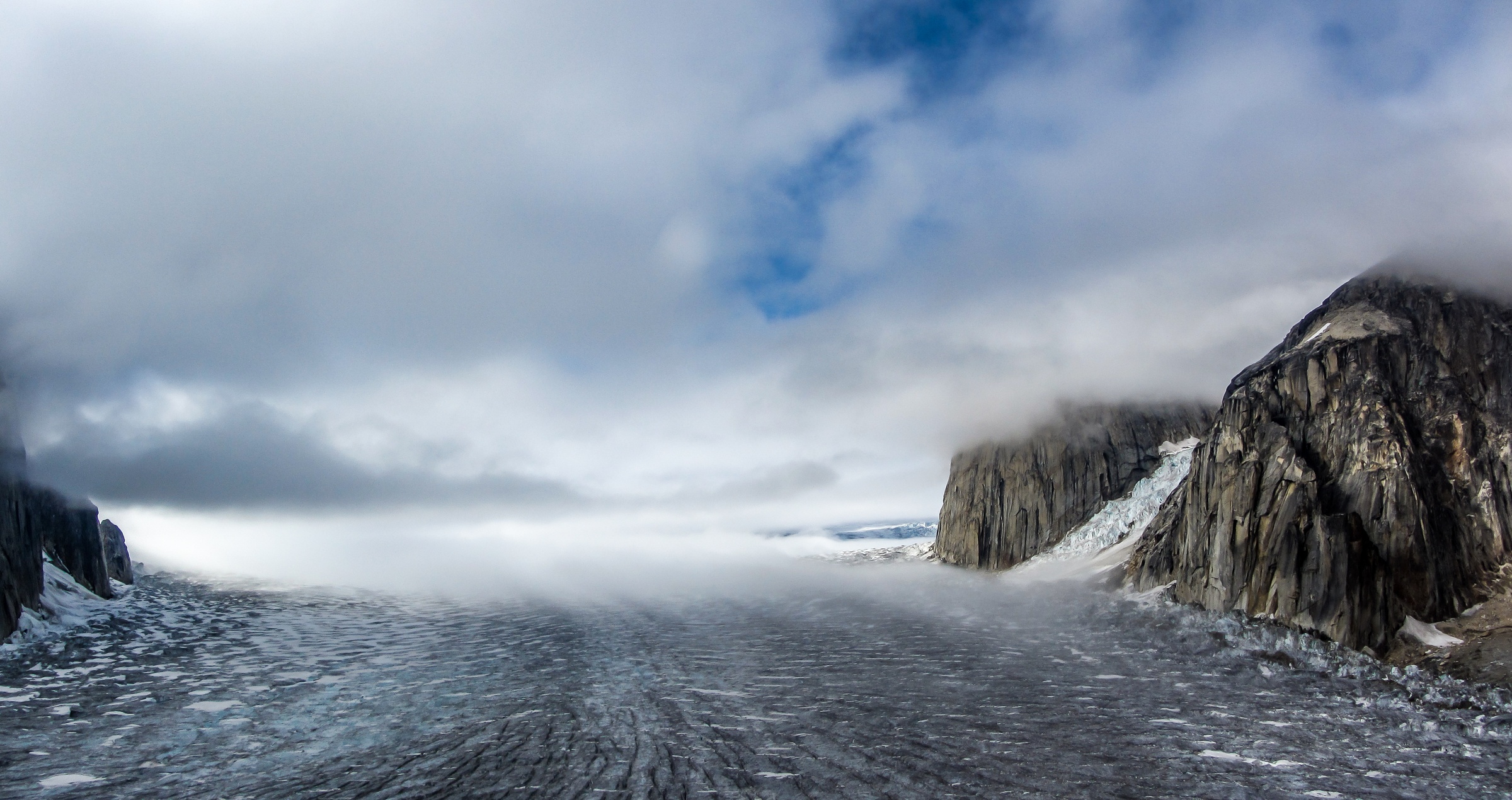 A rocky, snow-covered landscape extends toward a cloudy sky with a glimpse of blue.