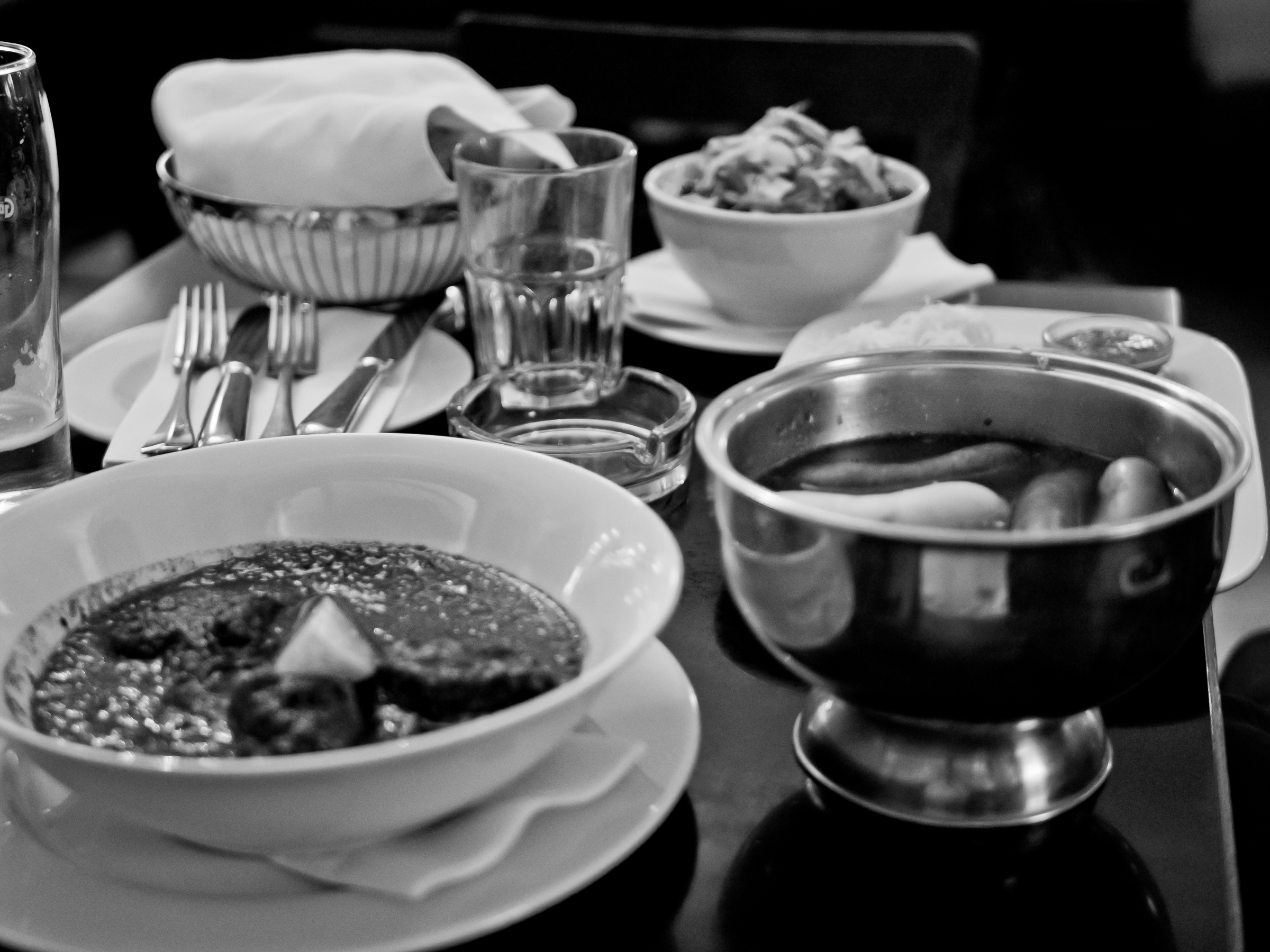 A table displays various bowls of food, glasses, silverware, and napkins in a dimly lit setting.