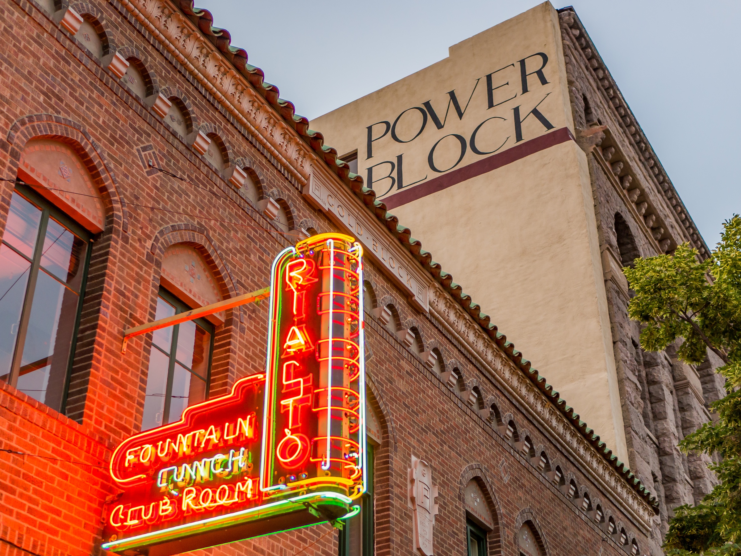 A neon sign for Fountain First Club Room hangs beside a brick building with Power Block signage.