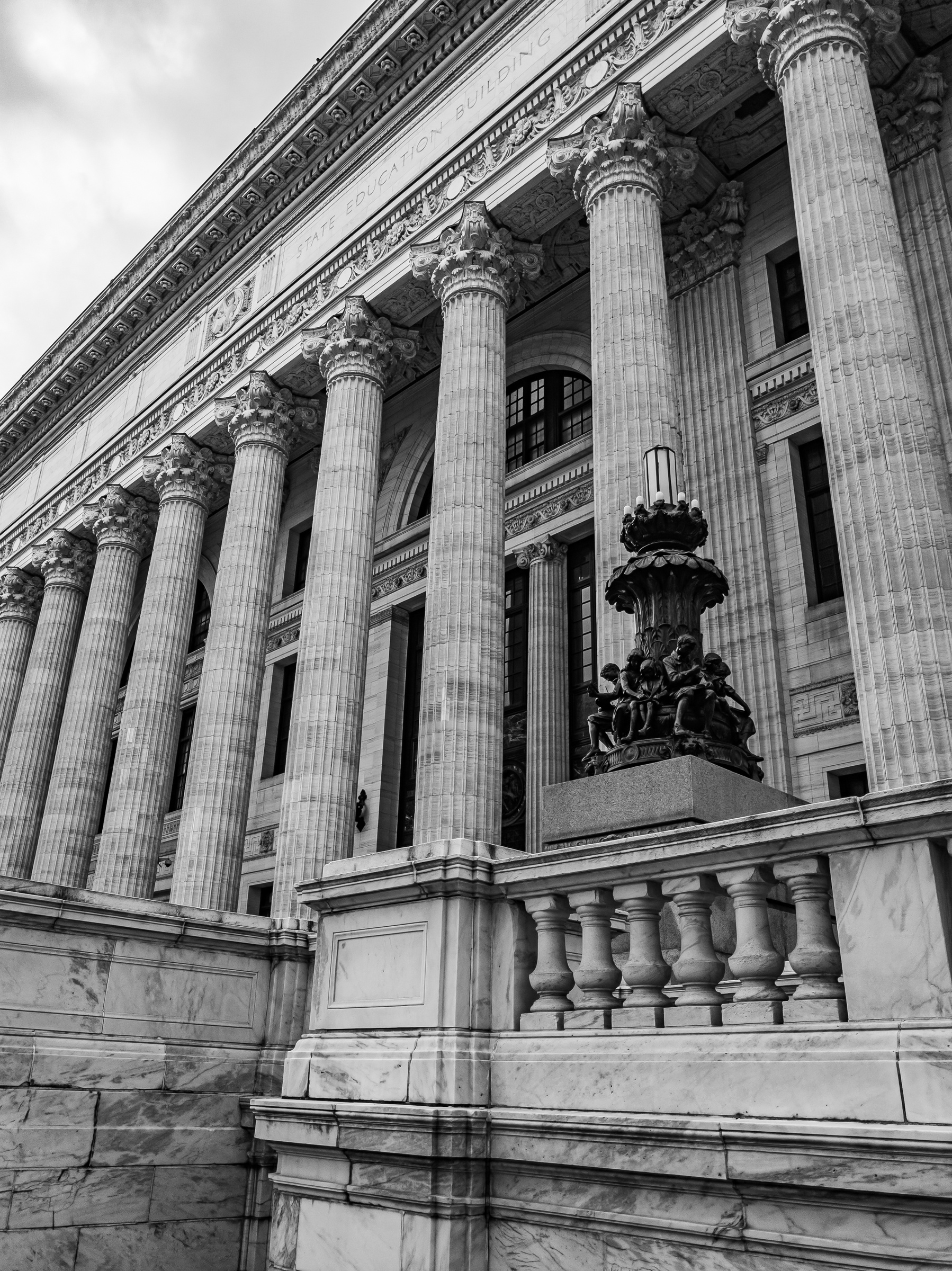 A grand neoclassical building with tall columns and a decorative fountain sits on a stone terrace.