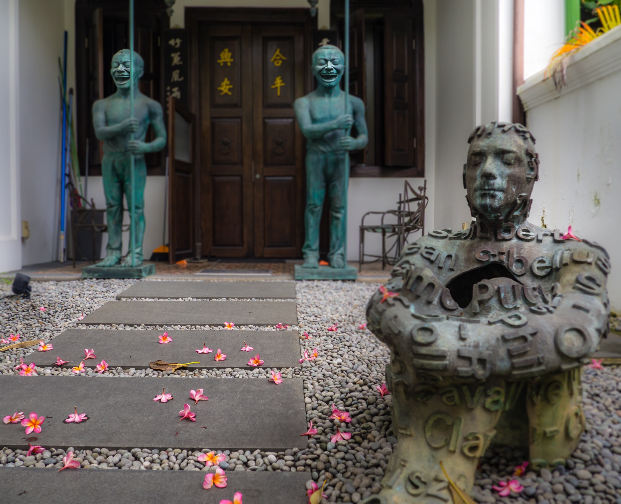 Bronze statues and a bust sit on a stone path in front of a traditional wooden building.