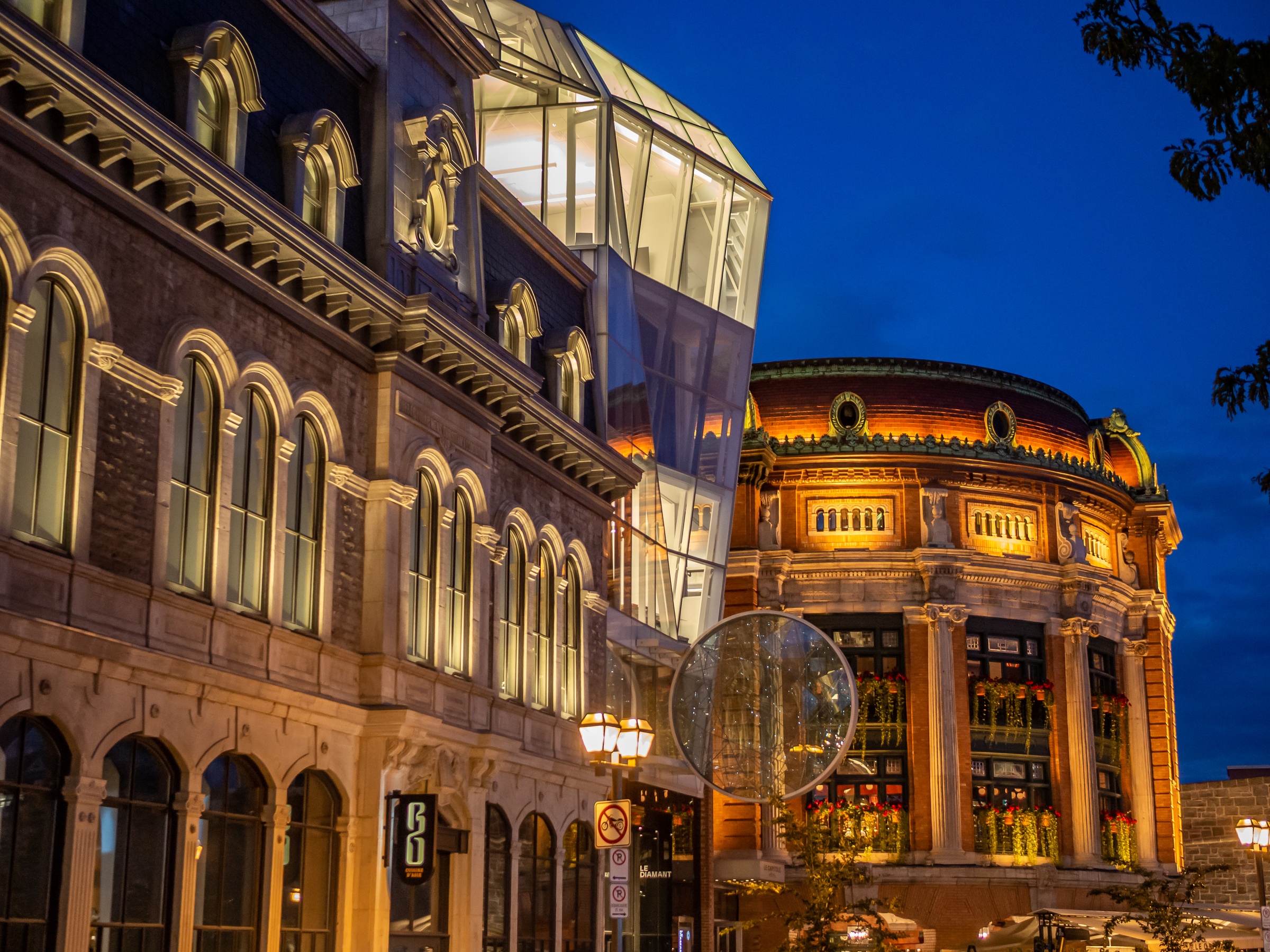 Illuminated historic buildings with modern architecture stand side-by-side at dusk.