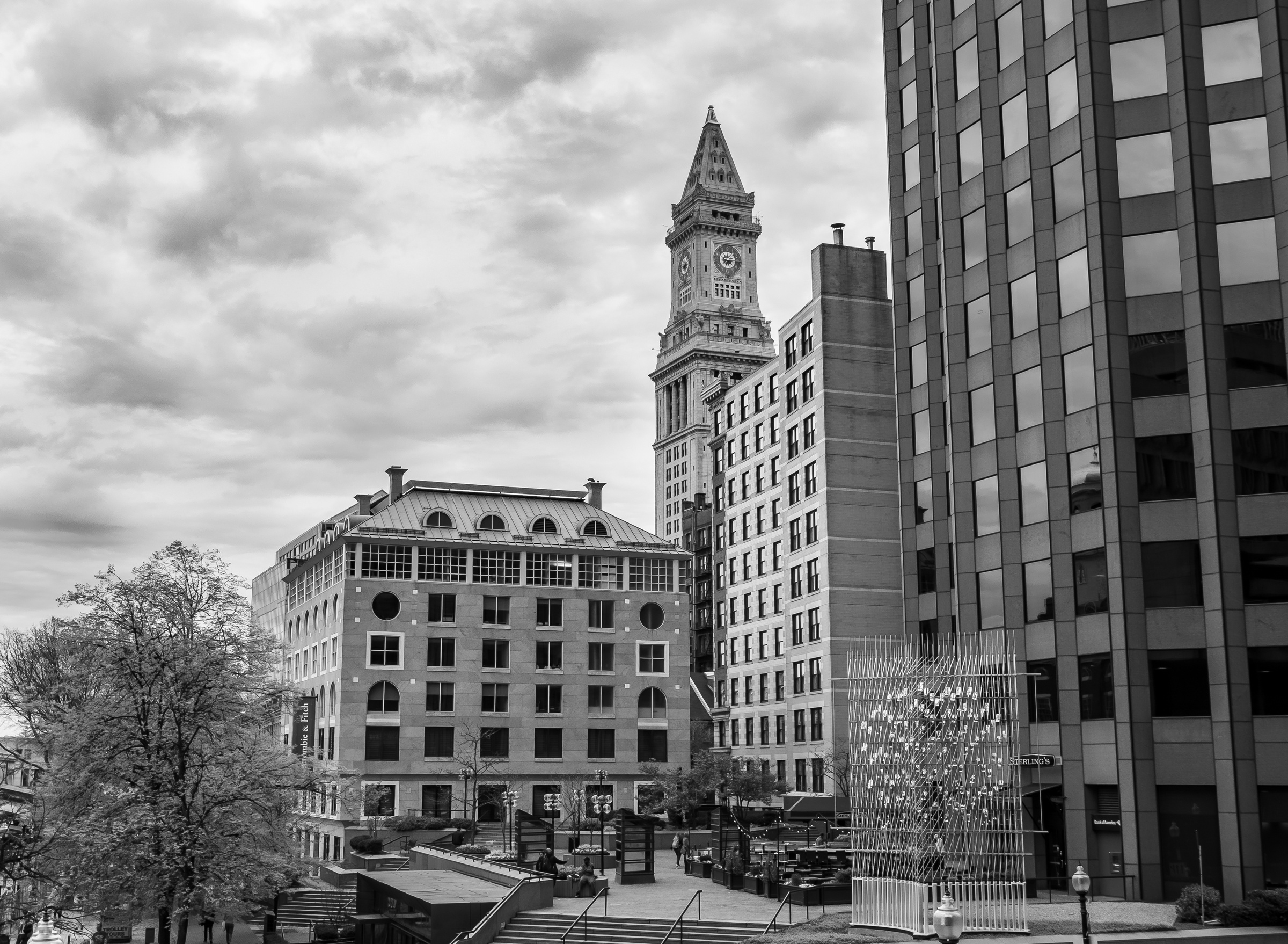 A clock tower and modern buildings stand beneath a cloudy sky in a city setting.