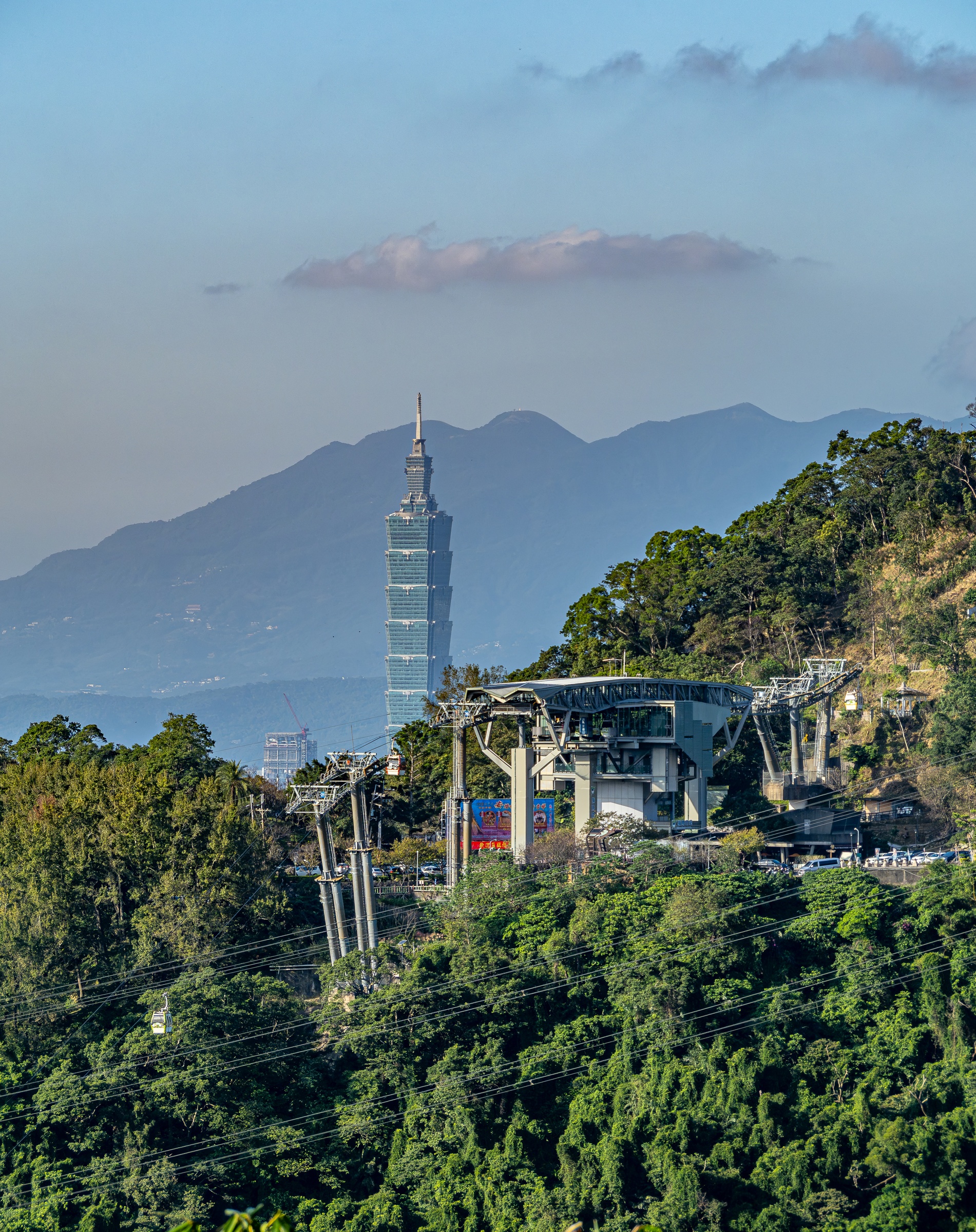 Taipei 101 skyscraper rises behind lush green hills and a cable car station.