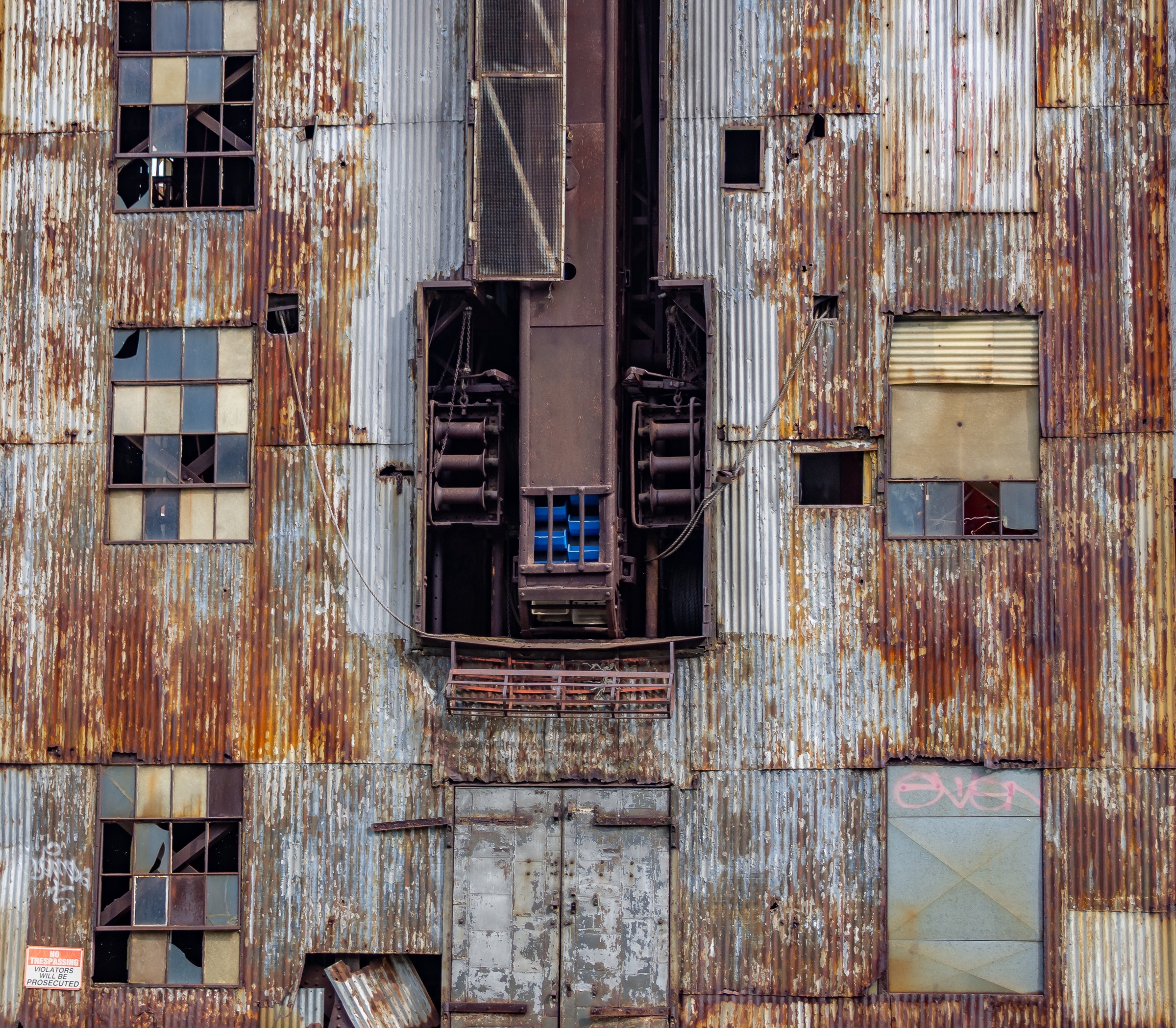 A rusted corrugated metal building with windows, doors, and industrial equipment is seen from above.