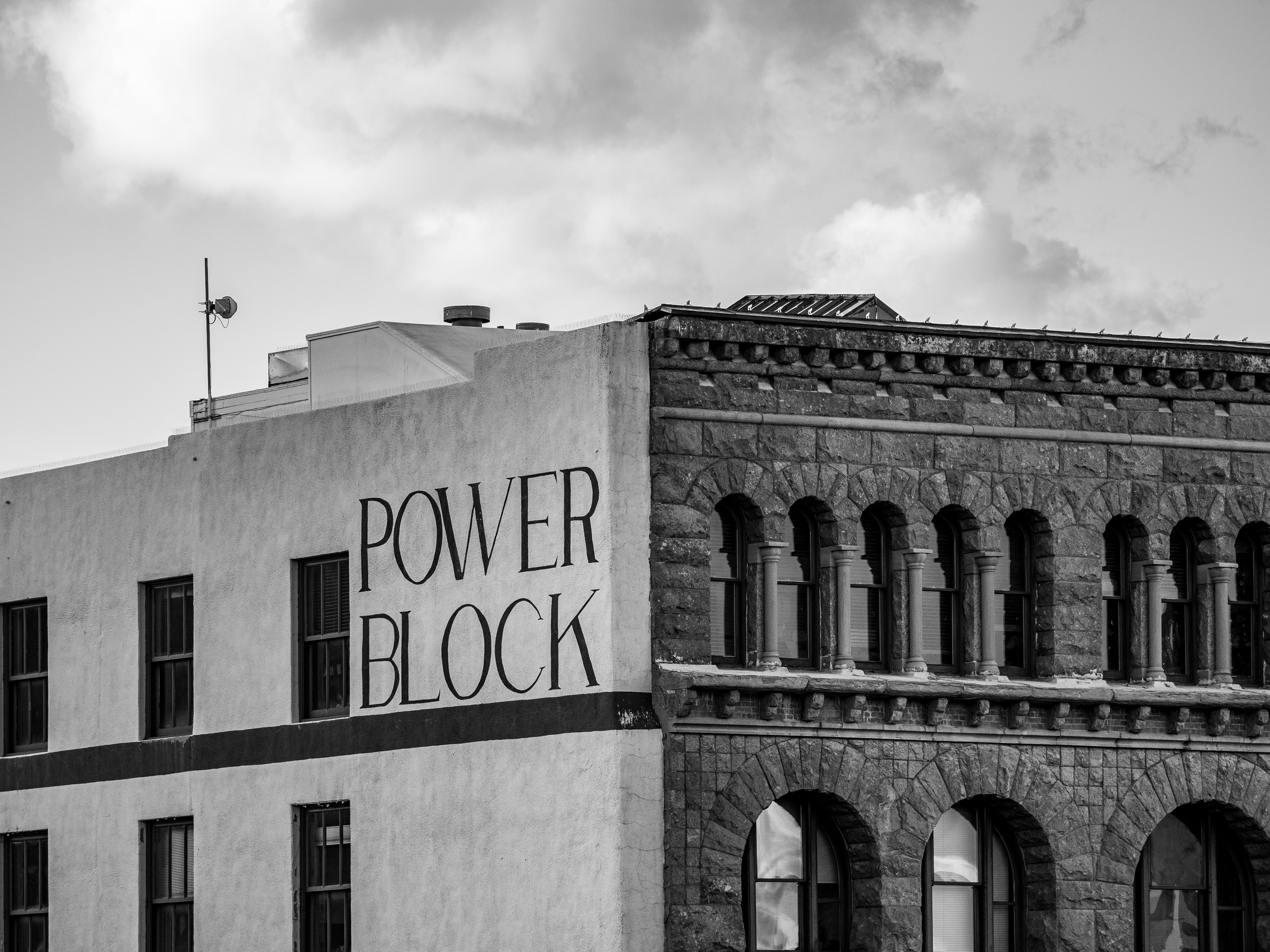 A black and white photograph shows a building with "Power Block" painted on its side, set against cloudy skies.