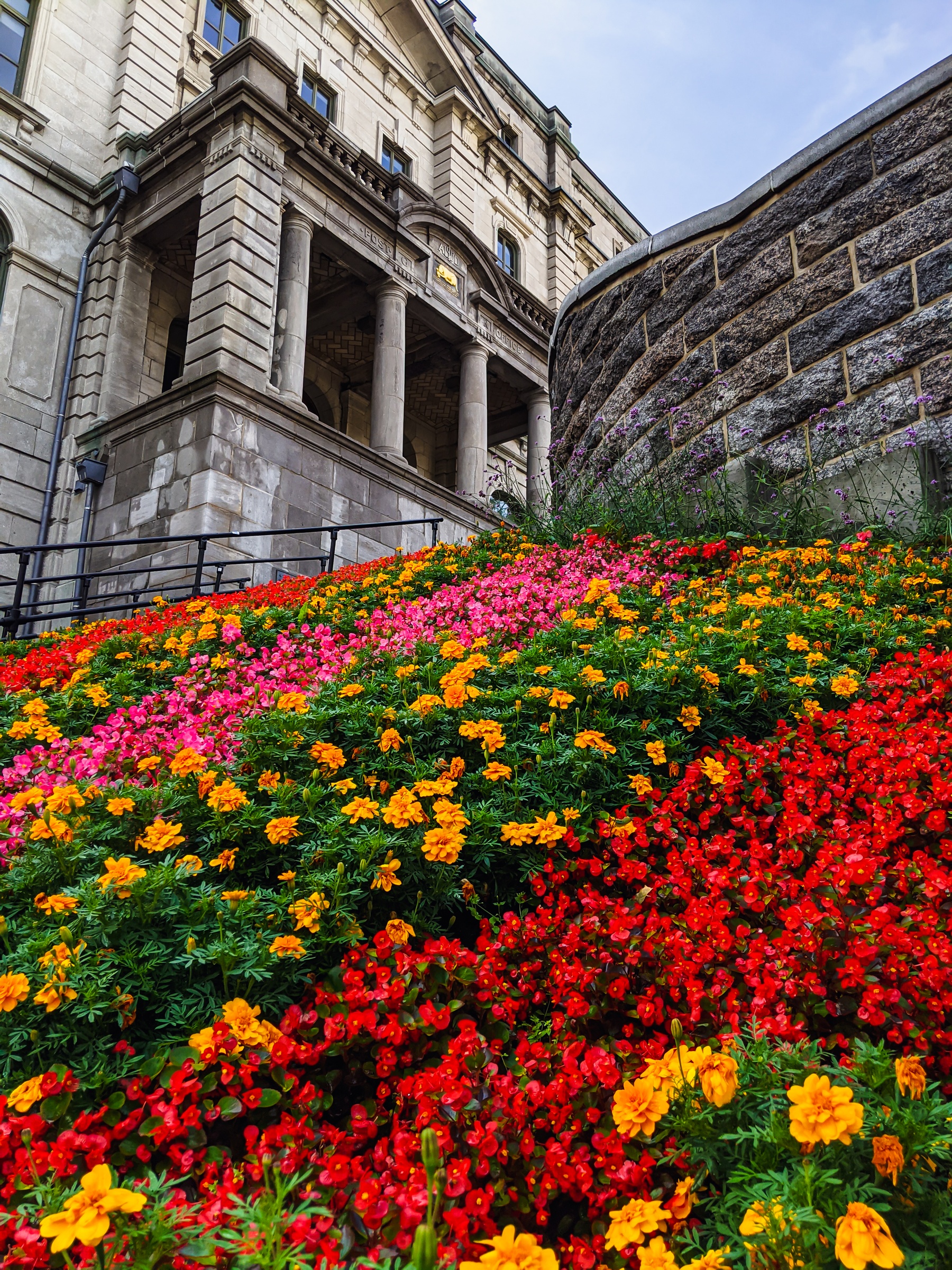 Colorful flowers bloom on a slope below a grand stone building with columns.