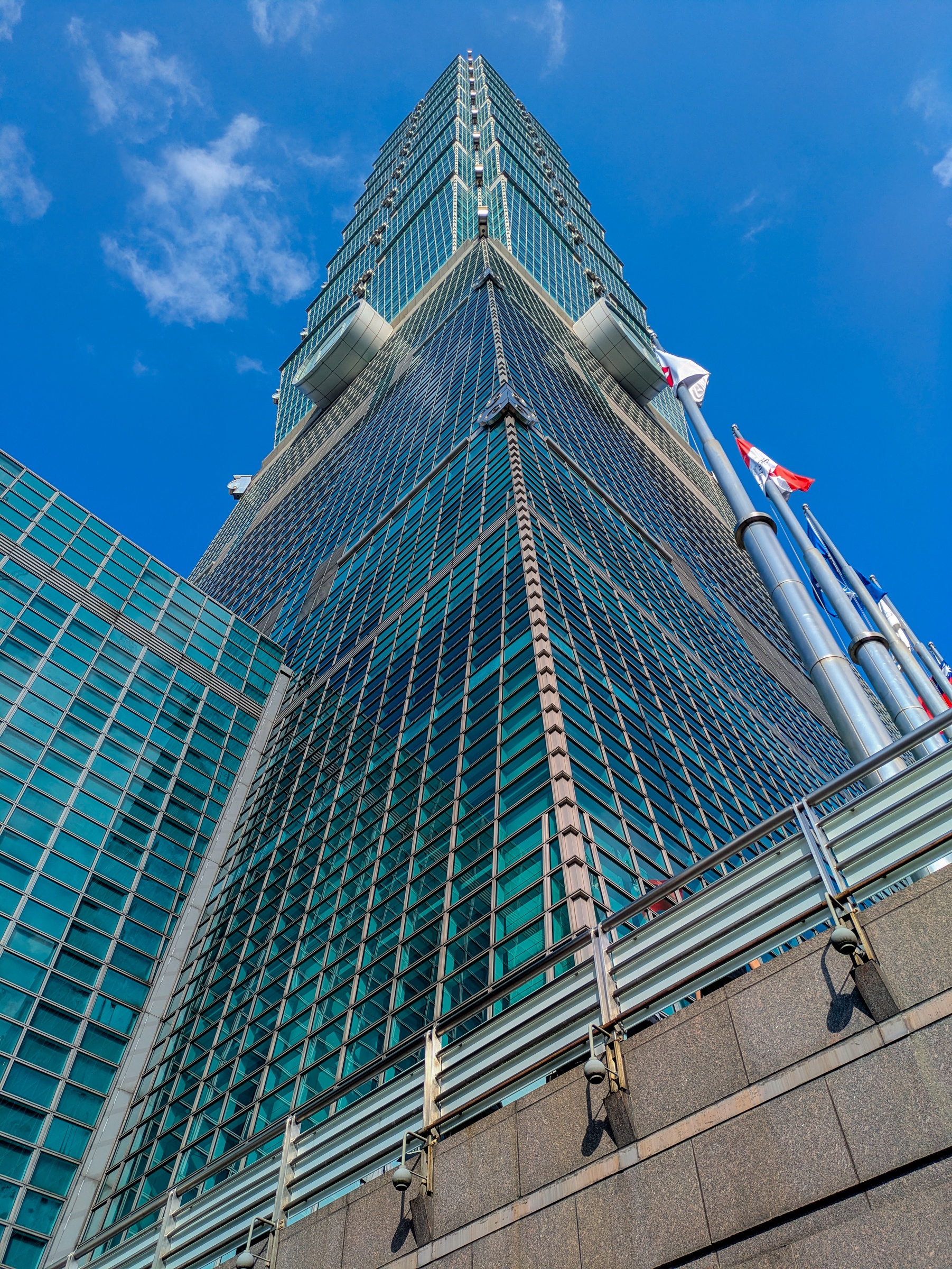 Taipei 101 skyscraper rises against a blue sky with scattered white clouds.