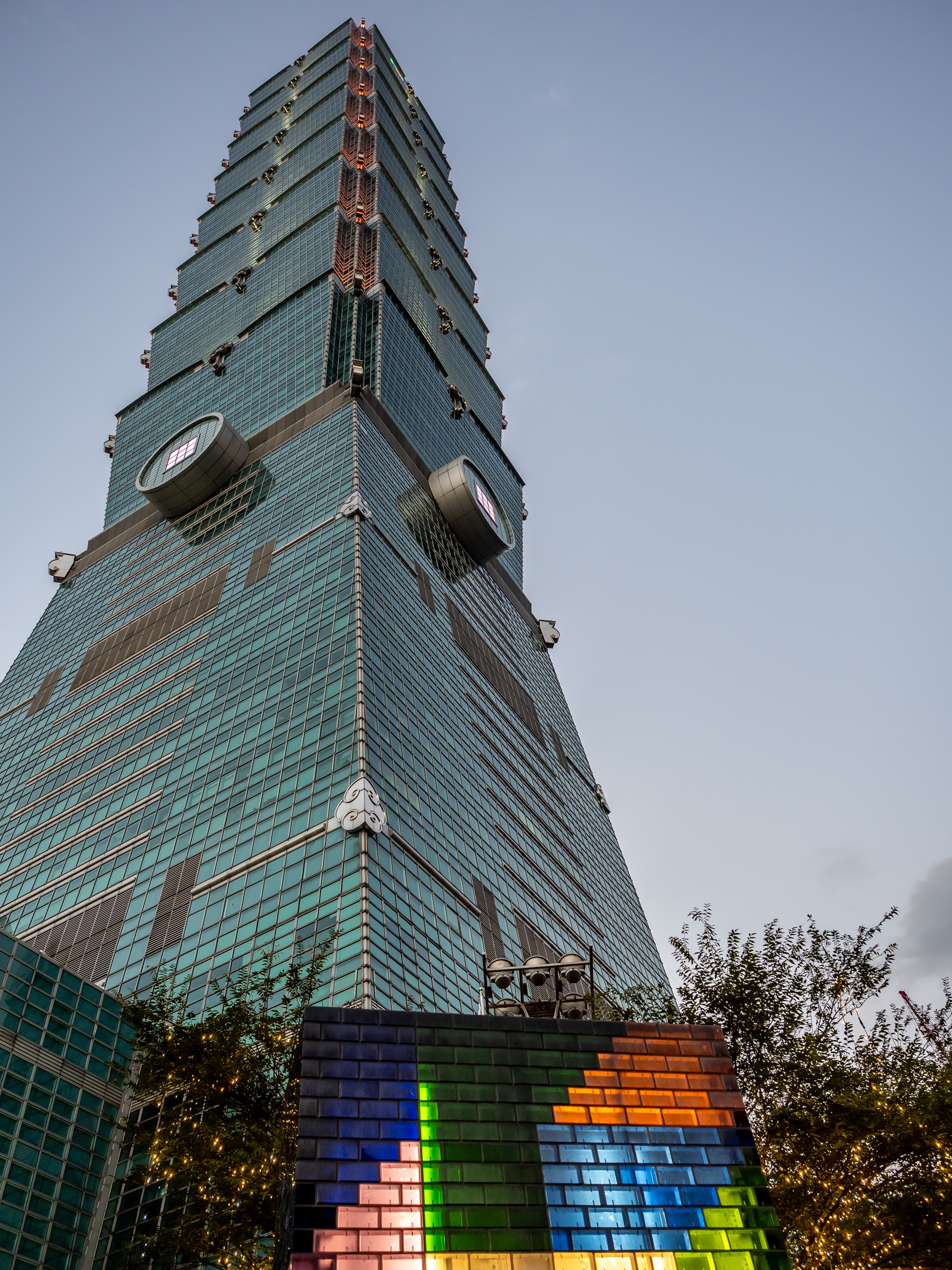 Taipei 101 skyscraper rises against a twilight sky, with a colorful mosaic at its base.