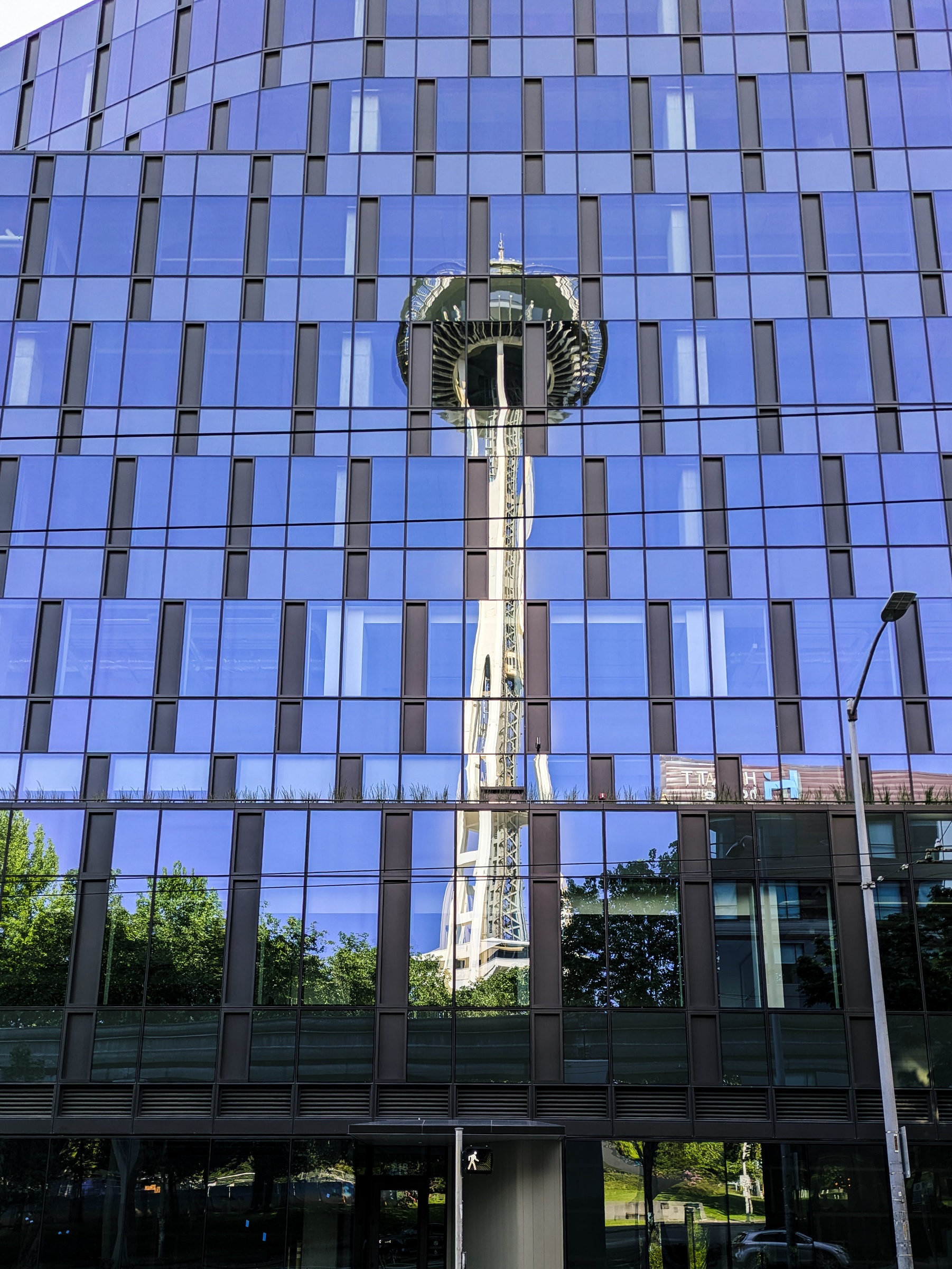 A modern glass building reflects the Seattle Space Needle and surrounding trees.