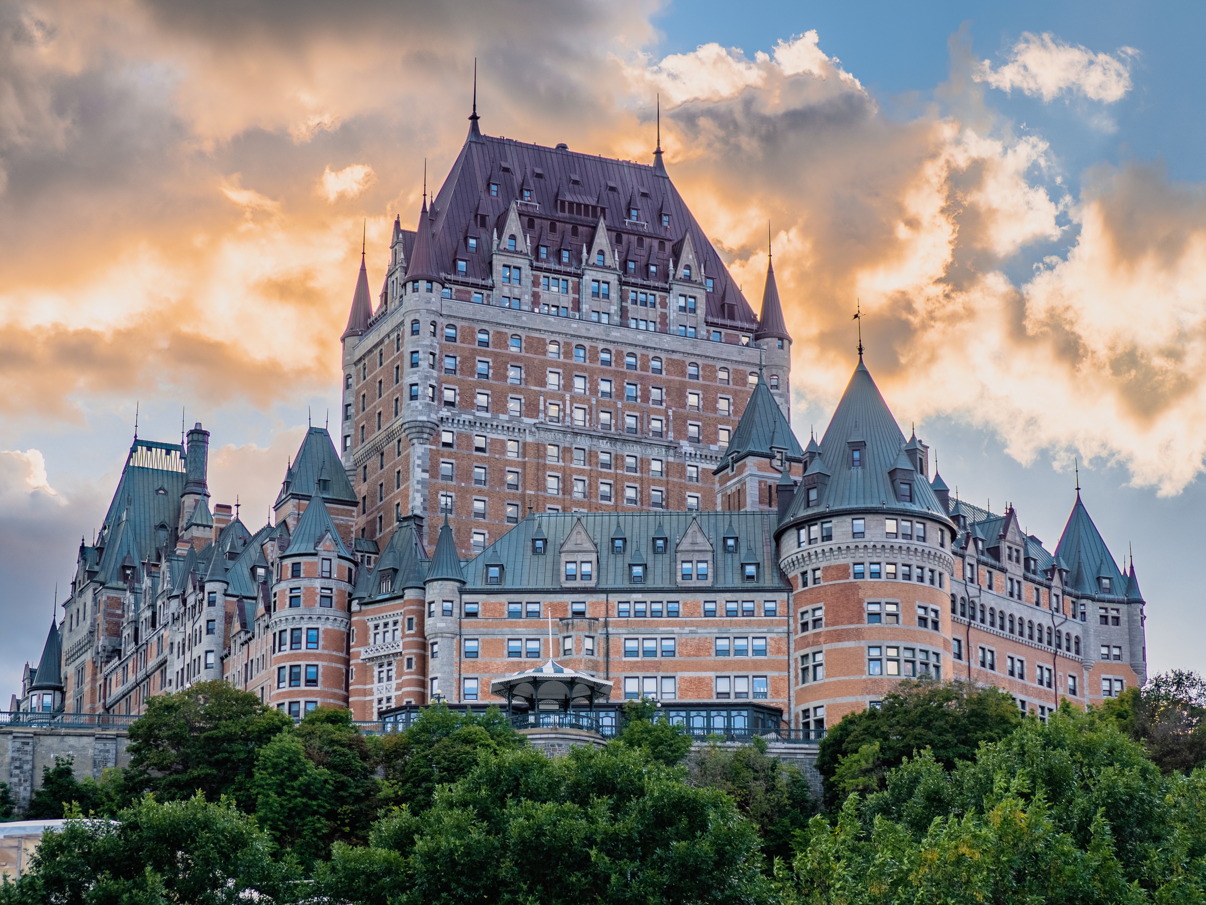 Château Frontenac, a grand hotel, sits atop a hill overlooking Quebec City under a cloudy sky.