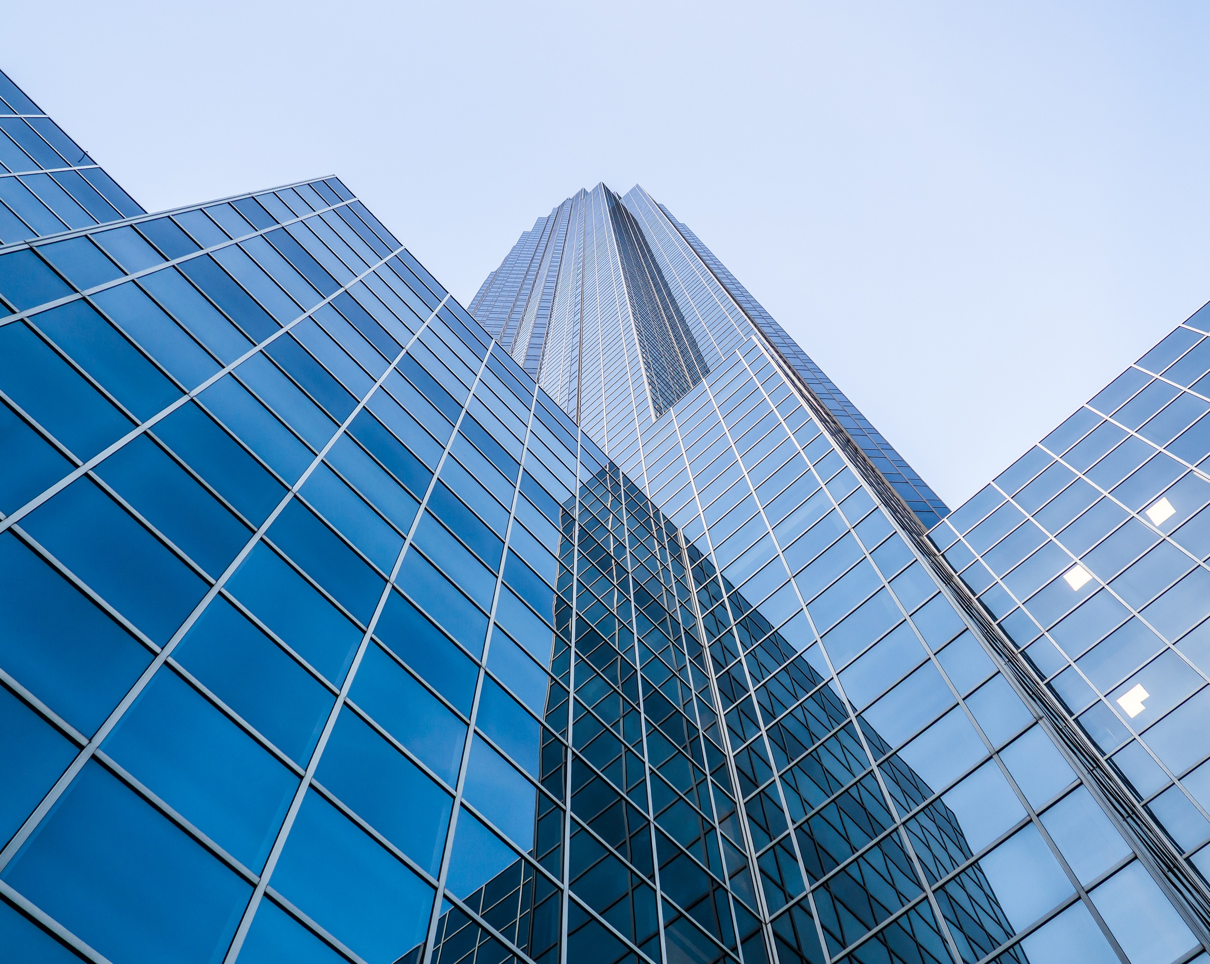 Modern glass skyscrapers reach upwards against a clear blue sky.