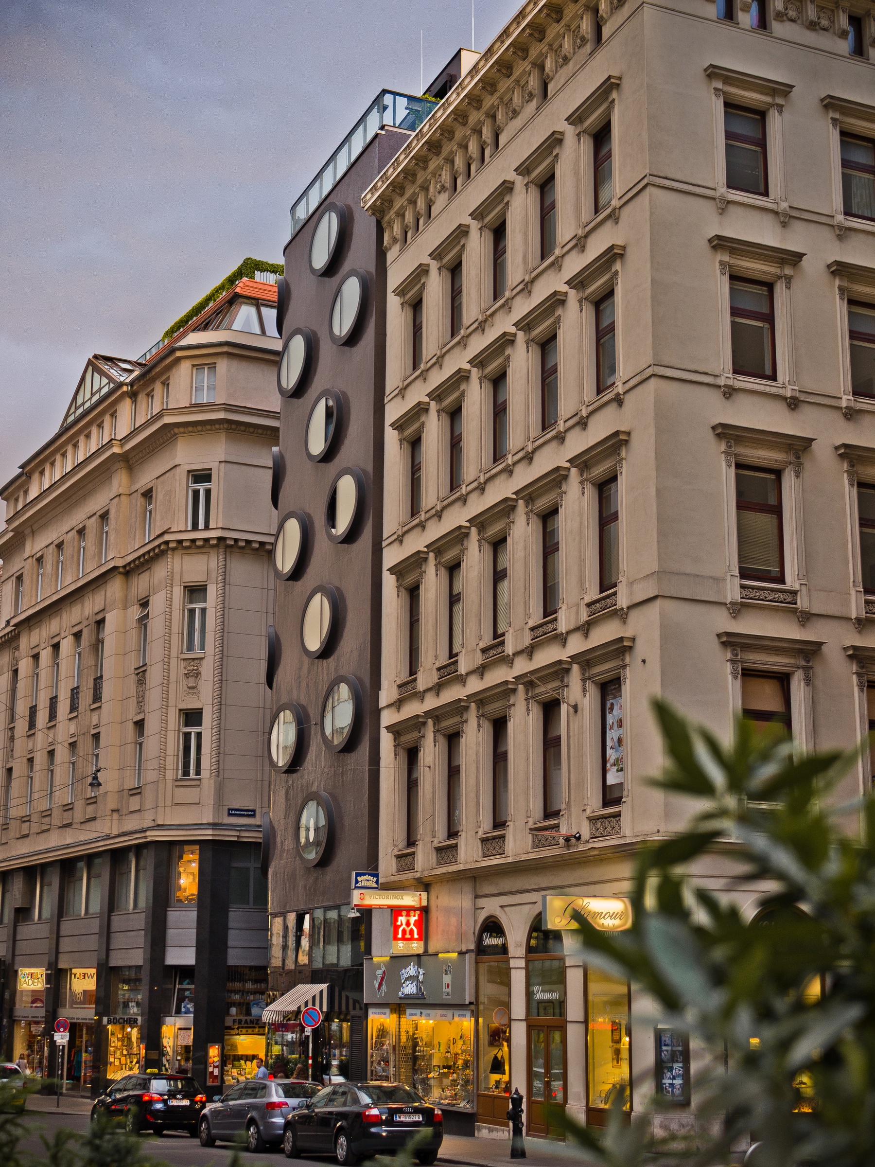 Modern building with circular windows stands between two traditional buildings on a city street.