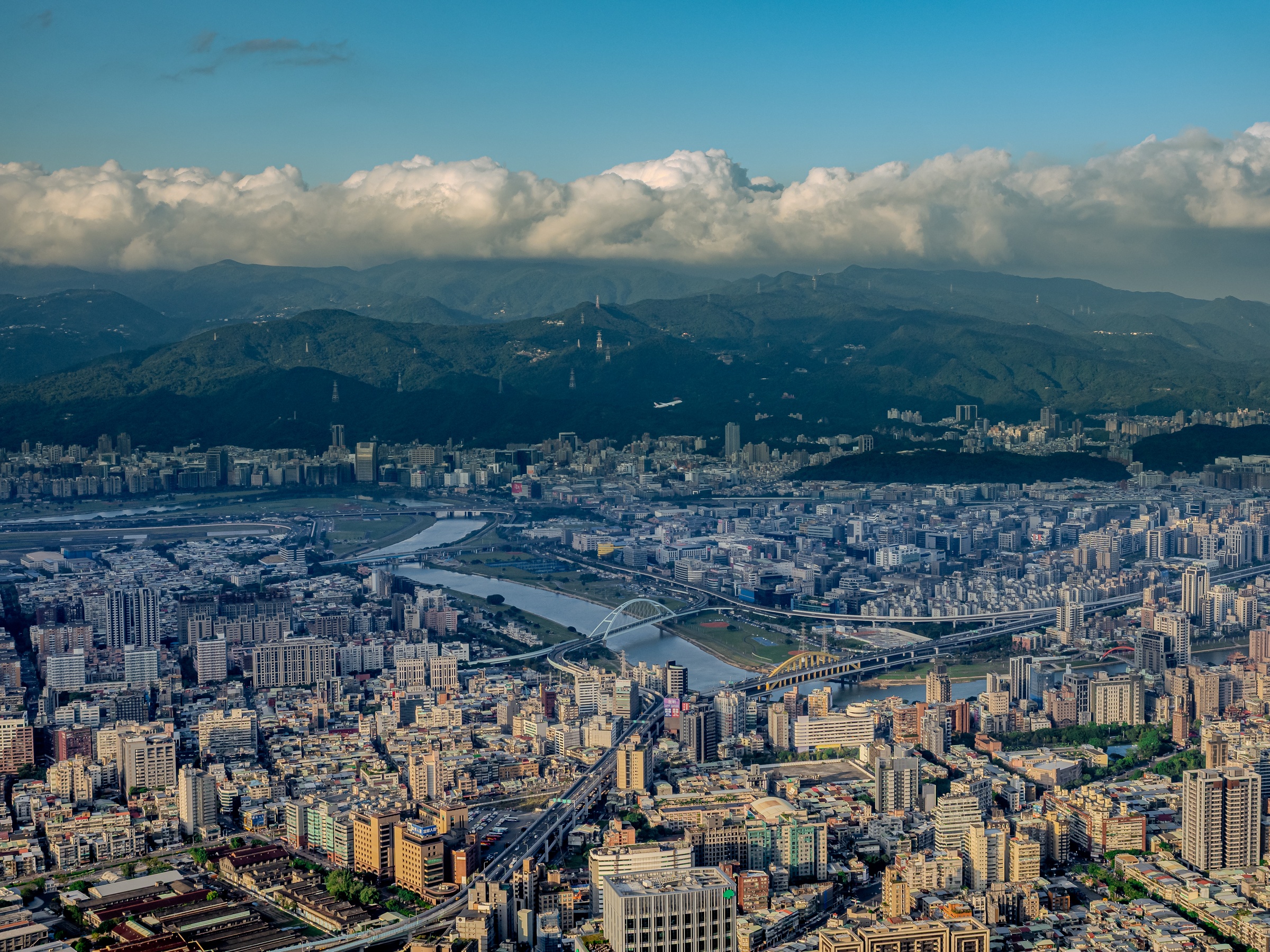 A sprawling city with dense buildings, a river, and rolling hills sits under a cloudy sky.
