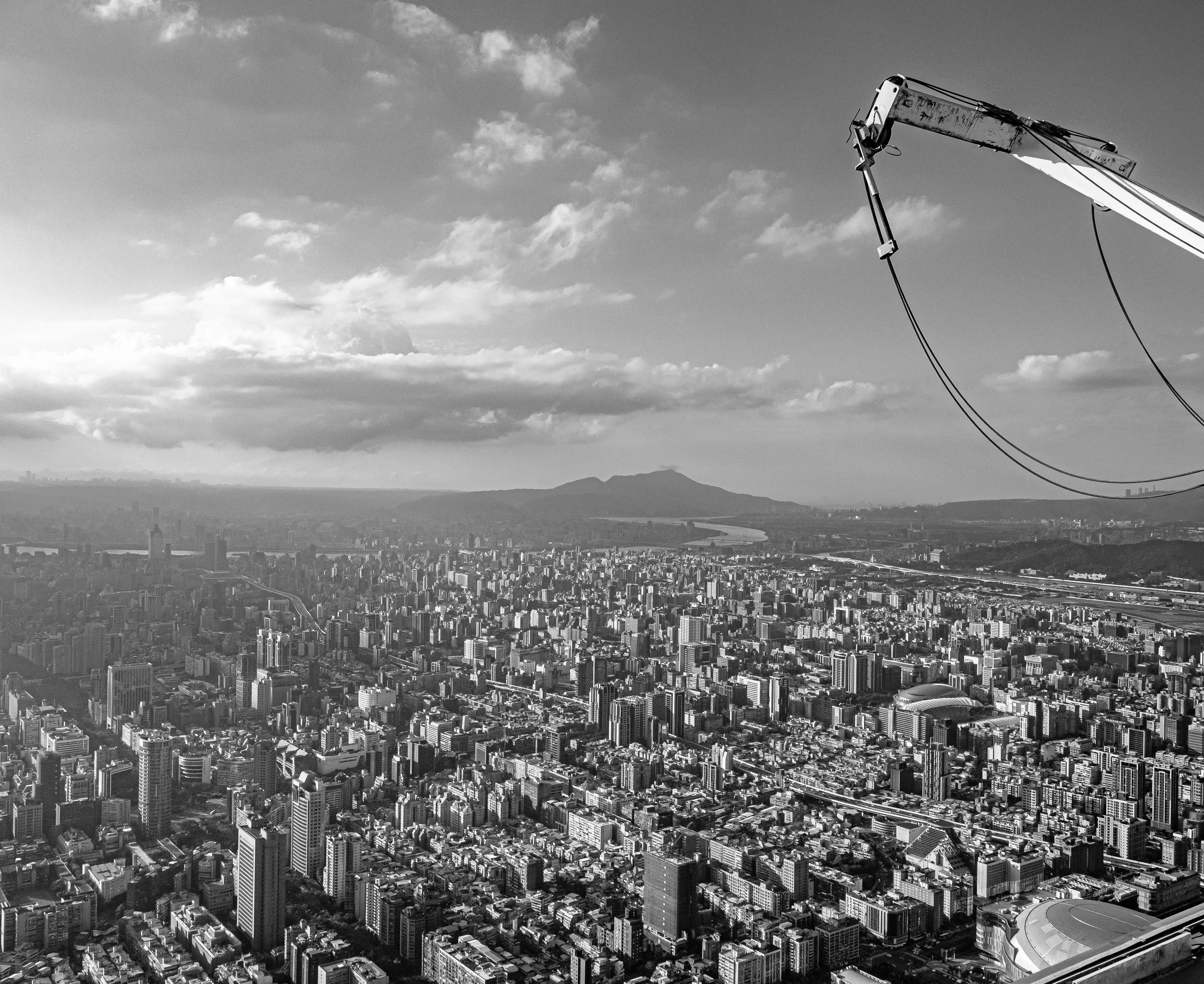 A crane extends over a sprawling cityscape with distant hills and cloudy skies.