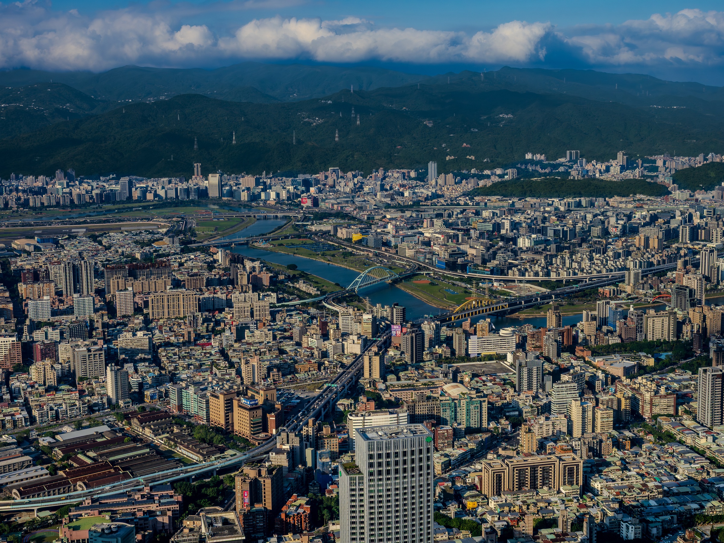 A sprawling urban landscape with a river and bridges stretches toward distant, rolling mountains.
