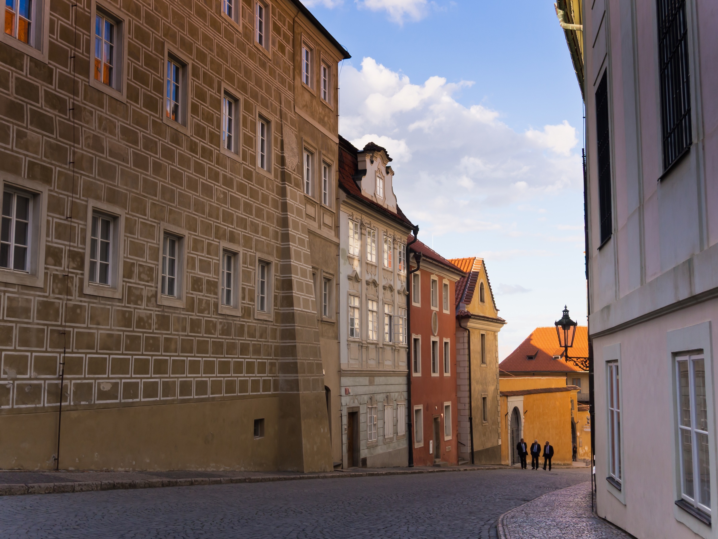 Cobblestone street leads past historic buildings with patterned facades and arched gateway in a European town.