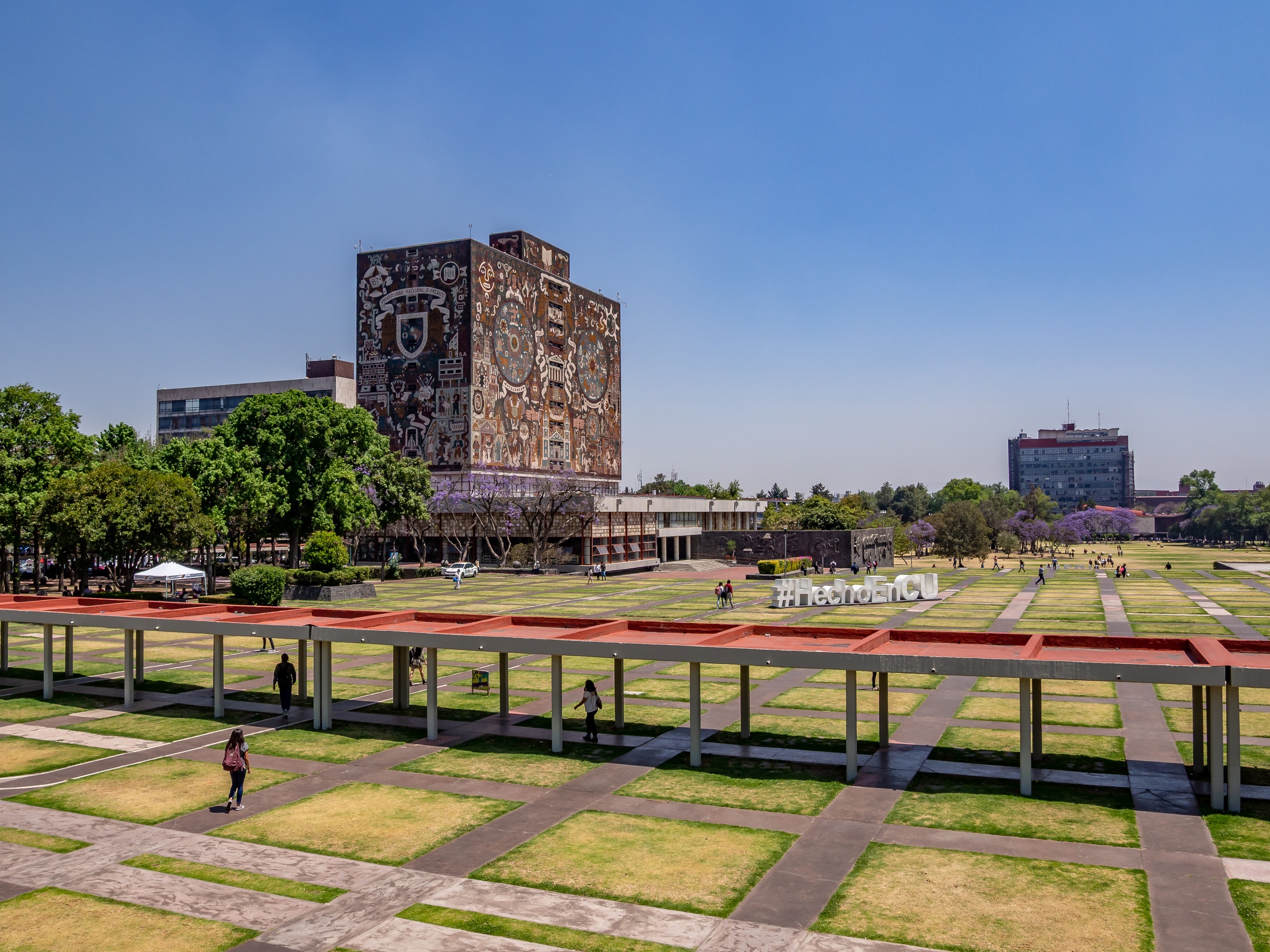 A large building with a mural stands in a sprawling green campus with modern architecture and walkways.
