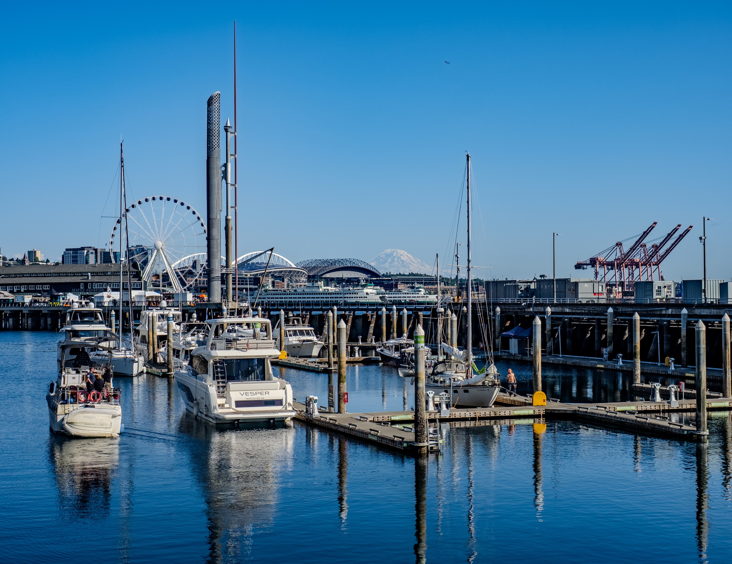 Boats are docked in a harbor with a Ferris wheel and cranes visible in the background.